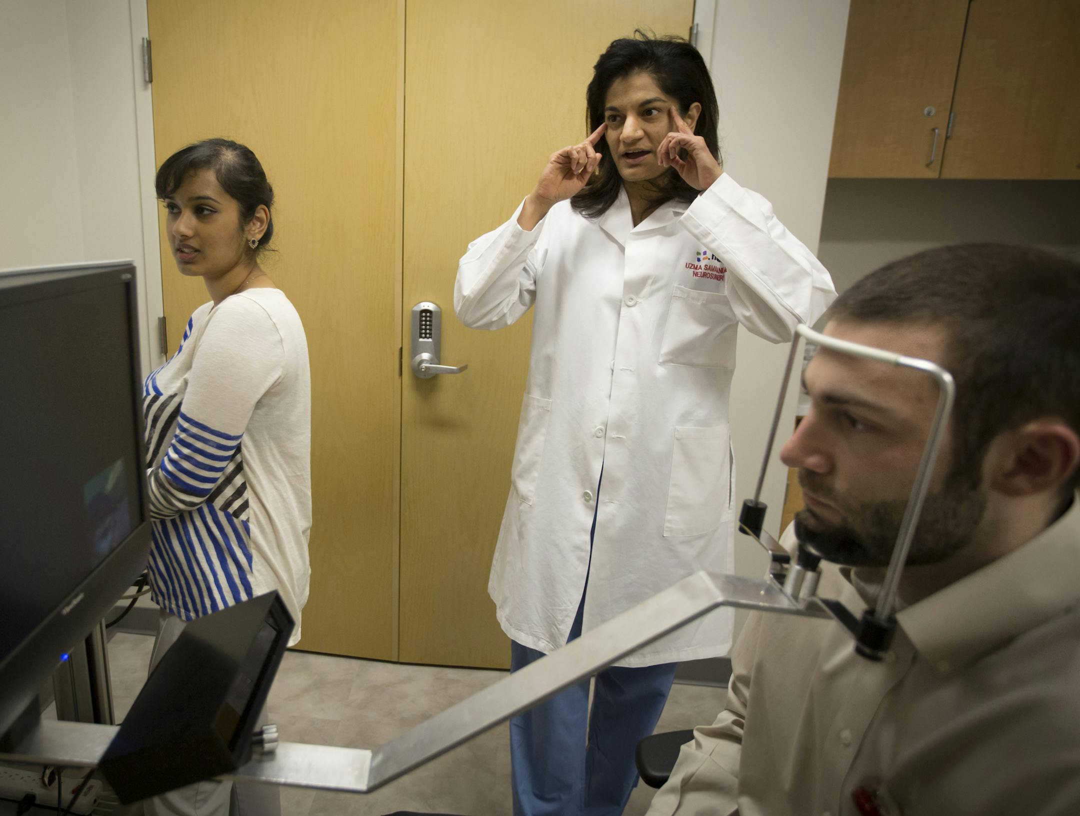 Dr. Uzma Samadani, middle, talked about eye movements as research assistant Sam Daly, right foreground, sat through an eye test conducted by senior project coordinator Vikalpa Dammavalam, left, at HCMC on Wednesday, March 9, 2016, in Minneapolis, Minn. HCMC has been conducting eye tests on study participants including Daly, who works in the lab and is a former athlete, as part of research to identify better ways to detect concussion injuries and their long-term consequences. The test tracks both