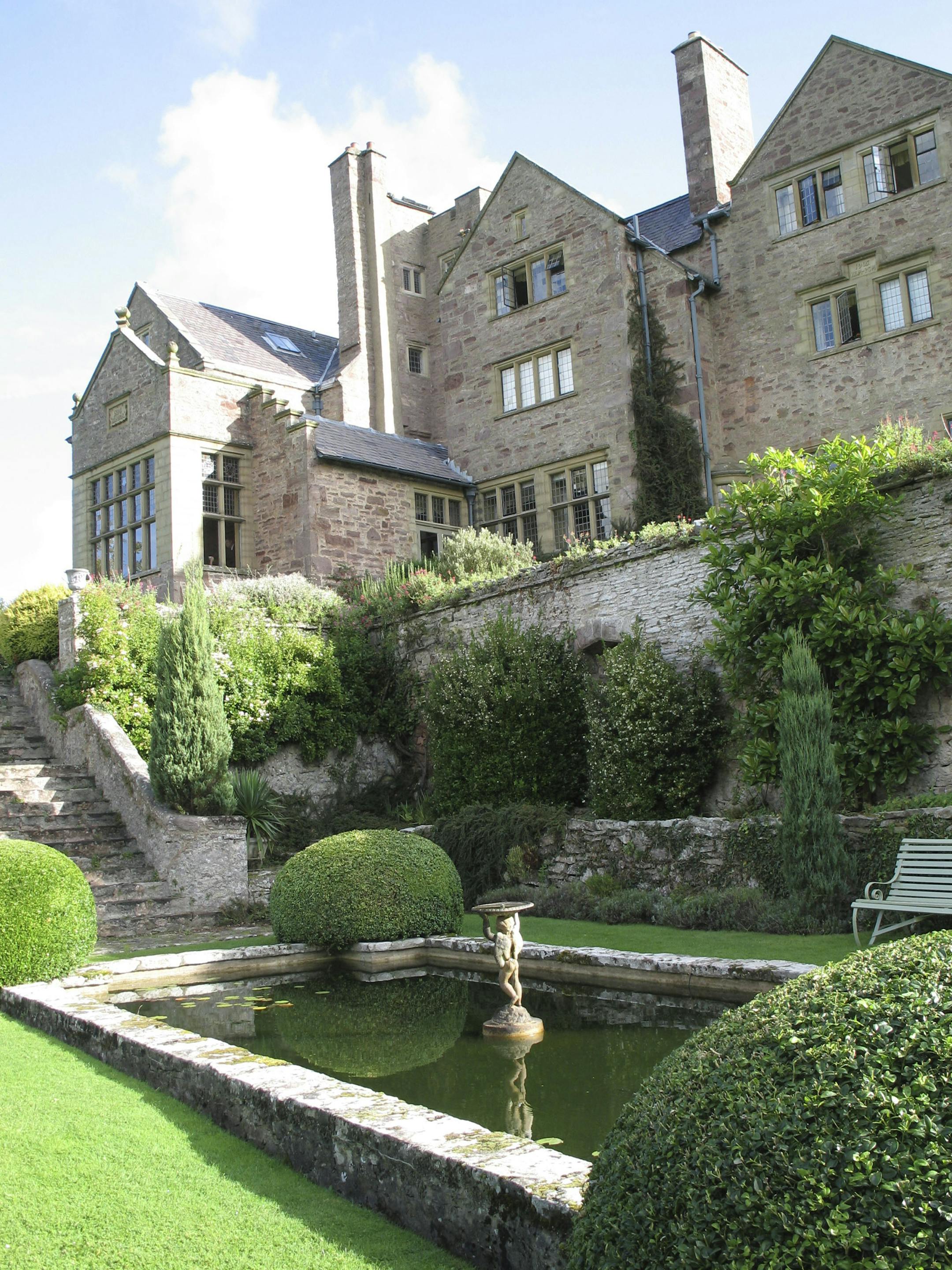 A lilypad pond with fountain decorates a garden below the main buildings of Bodysgallen Hall country house hotel in North Wales. The pink limestone buildings cup a 13th-century watchtower built to protect Conwy Castle two miles away.