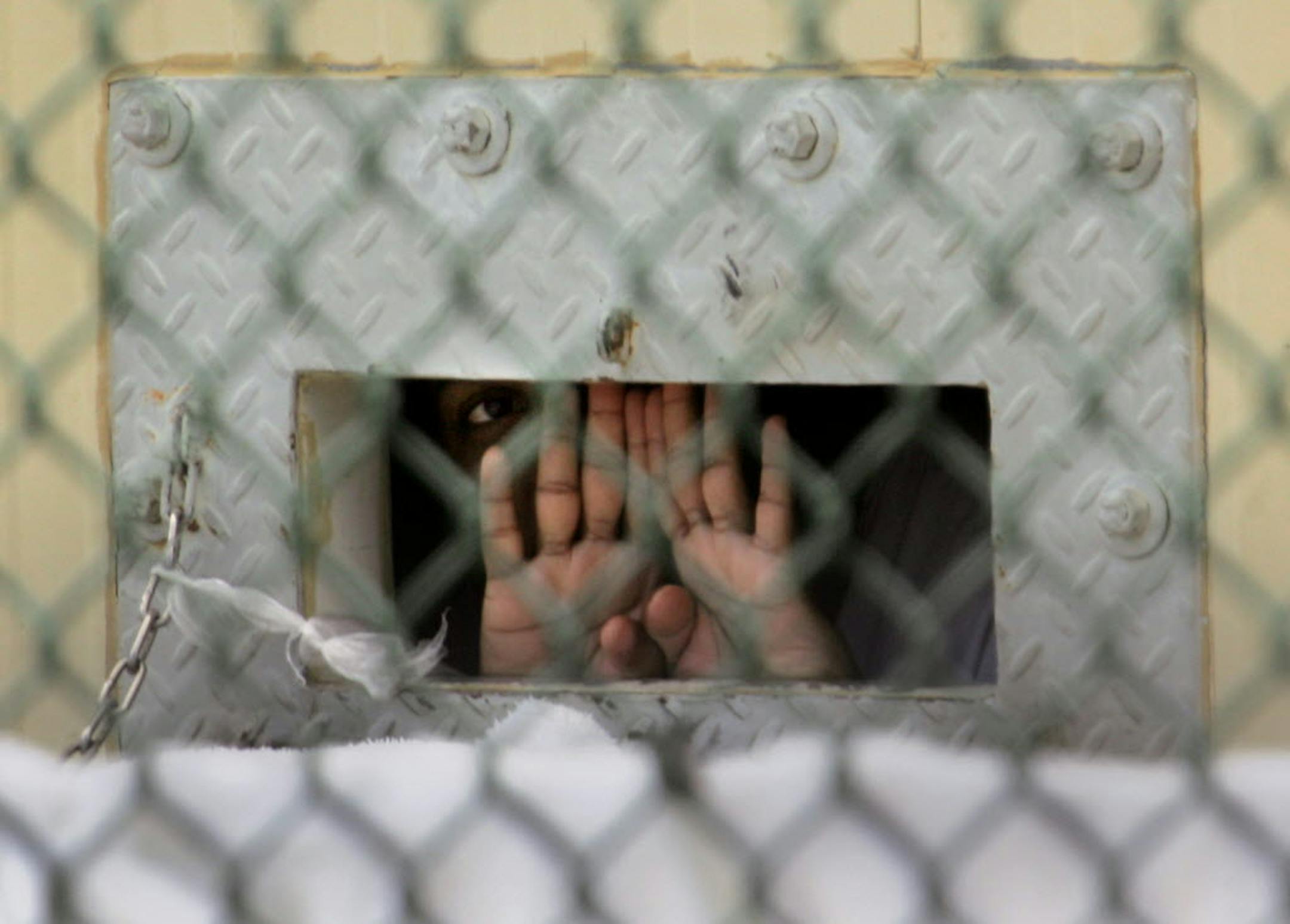 A detainee shields his face as he peers out through the so-called "bean hole" which is used to pass food and other items into detainee cells at the Guantanamo Bay U.S. Naval Base, Cuba.