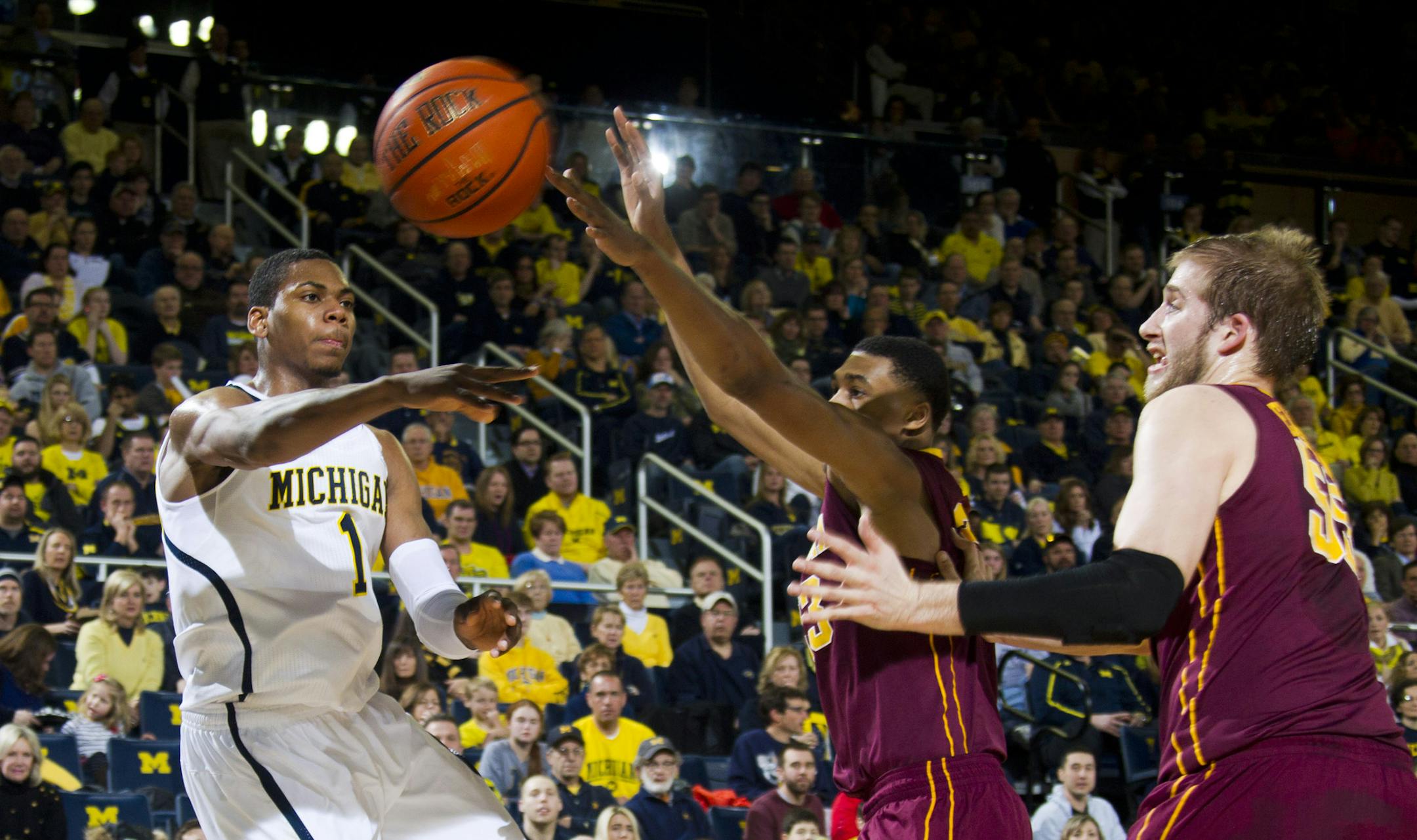 Michigan forward Glenn Robinson III (1) passes the ball past Minnesota forward Charles Buggs, middle, and center Elliott Eliason during the first half of an NCAA college basketball game at Crisler Center in Ann Arbor, Mich., Saturday, March 1, 2014. (AP Photo/Tony Ding)
