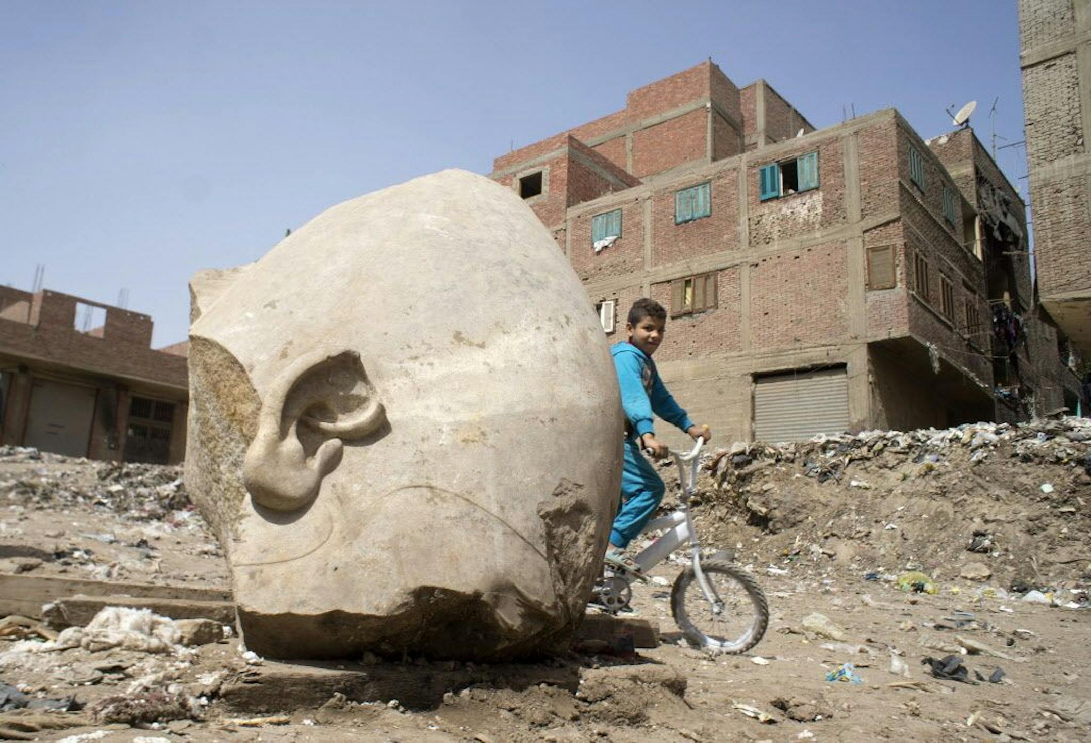 A boy rides his his bicycle past a recently discovered statue in a Cairo slum that may be of pharaoh Ramses II, in Cairo, Egypt, Friday, March 10, 2017. Archeologists in Egypt have discovered a massive statue that may be of pharaoh Ramses II, one of the country's most famous ancient rulers. The colossus, whose head was pulled from mud and groundwater by a bulldozer on Thursday, is around eight meters (yards) tall and was discovered by a German-Egyptian team.