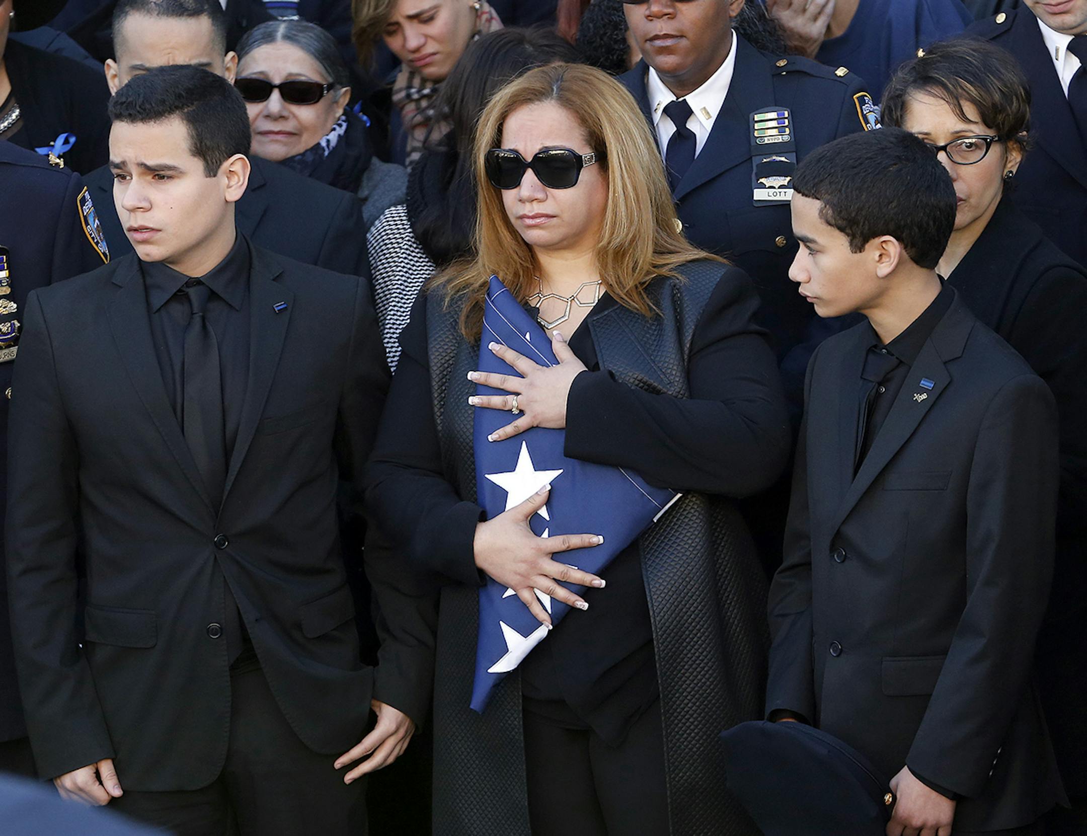 Maritza Ramos, center, widow of New York City police officer Rafael Ramos, holds a flag while standing with her two sons, Justin Ramos, left, and Jaden Ramos, following funeral services for officer Ramos at Christ Tabernacle Church, in the Glendale section of Queens, Saturday, Dec. 27, 2014, in New York. Ramos and his partner, officer Wenjian Liu, were killed Dec. 20 as they sat in their patrol car on a Brooklyn street. The shooter, Ismaaiyl Brinsley, later killed himself. (AP Photo/Julio Cortez