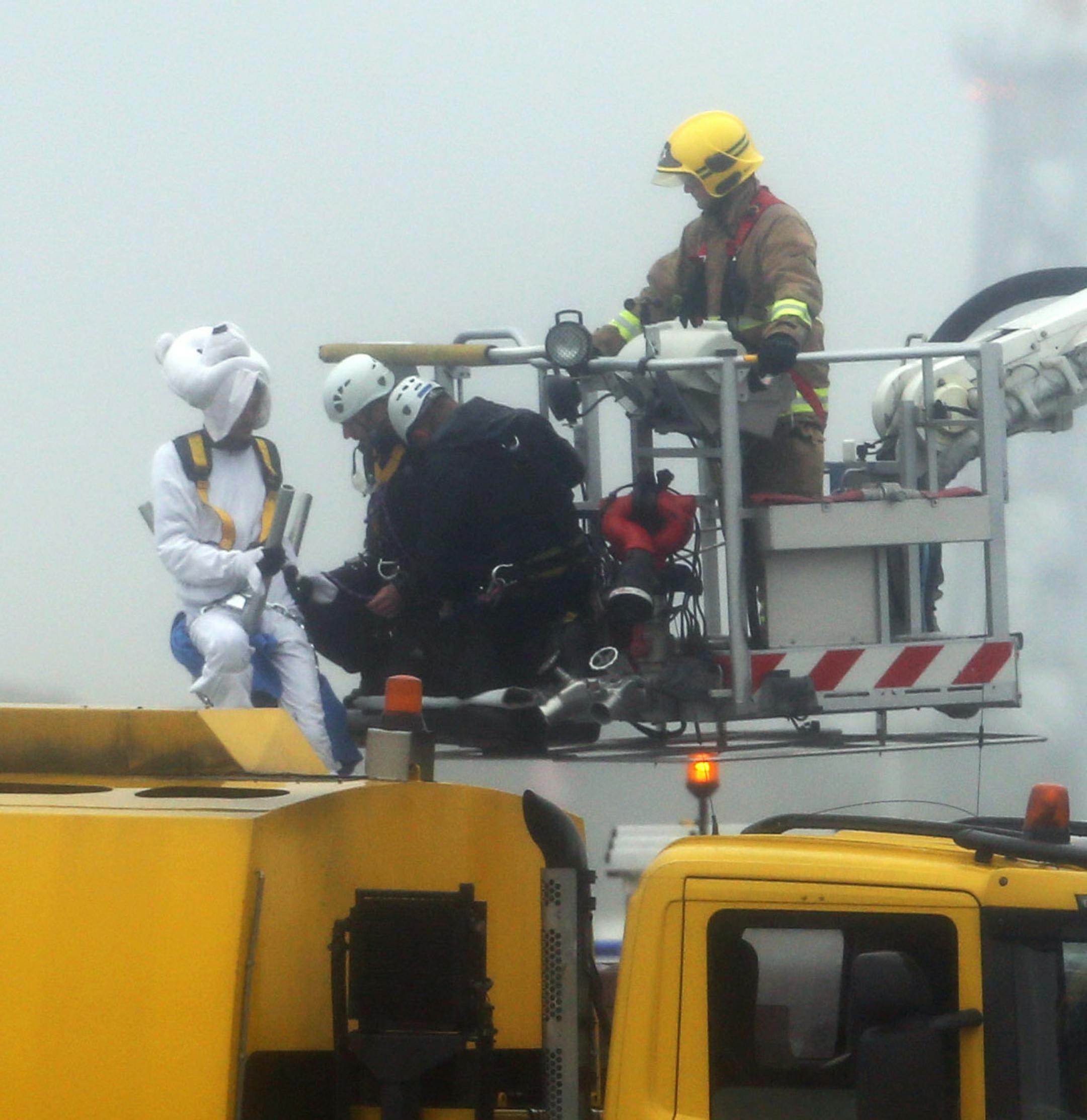Emergency service workers talk to an activist, dressed as a teddy bear, top left, from the pressure group Plane Stupid, who was one of several demonstrators who occupied the north runway at London's Heathrow Airport to launch a protest Monday July 13, 2015. A spokesman for the action group said a dozen demonstrators cut through a fence and entered the runway early on Monday. (Steve Parsons/PA via AP) UNITED KINGDOM OUT NO SALES NO ARCHIVE