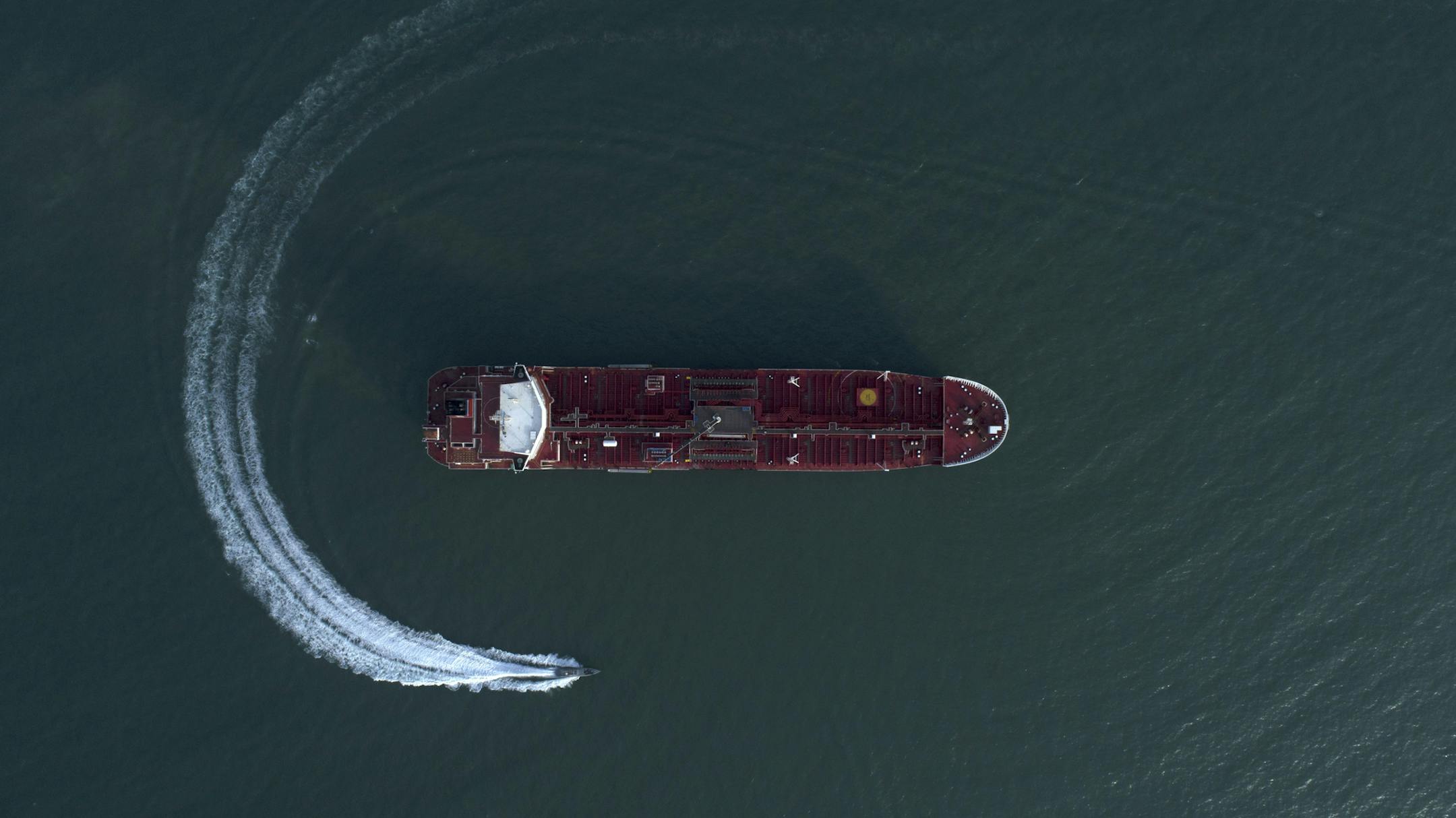 In this Sunday, July 21, 2019 photo, an aerial view shows a speedboat of Iran's Revolutionary Guard moving around the British-flagged oil tanker Stena Impero which was seized in the Strait of Hormuz on Friday by the Guard, in the Iranian port of Bandar Abbas. Global stock markets were subdued Monday while the price of oil climbed as tensions in the Persian Gulf escalated after Iran's seizure of a British oil tanker on Friday. (Morteza Akhoondi/Tasnim News Agency via AP)