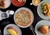 A selection of Altera's brunch items, shot overhead with an egg sandwich, giant hash brown, omelette, scrambled eggs on toast, a latte colored golden with tumeric and a salad.