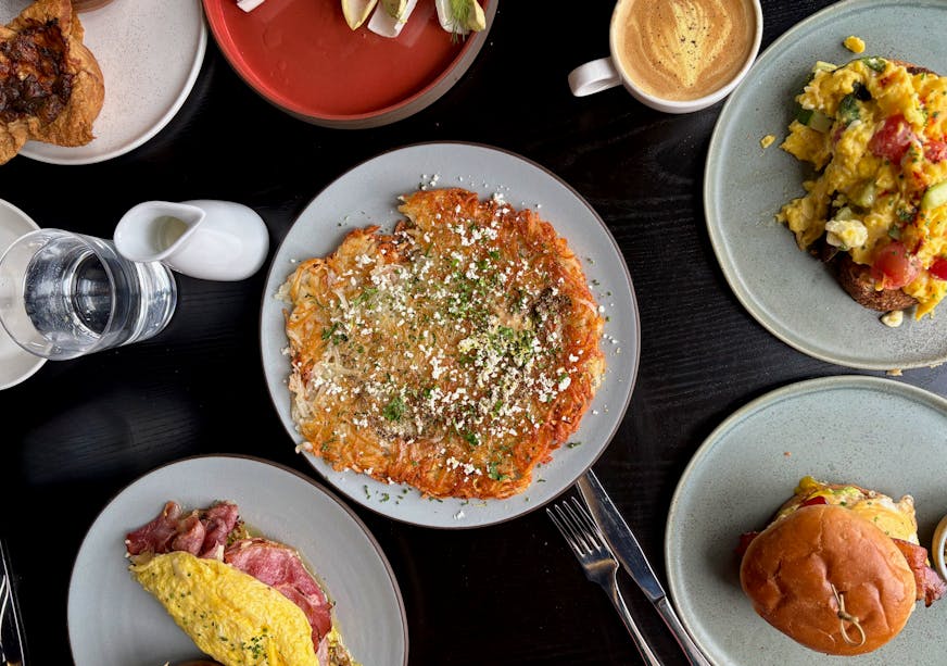 A selection of Altera's brunch items, shot overhead with an egg sandwich, giant hash brown, omelette, scrambled eggs on toast, a latte colored golden with tumeric and a salad.