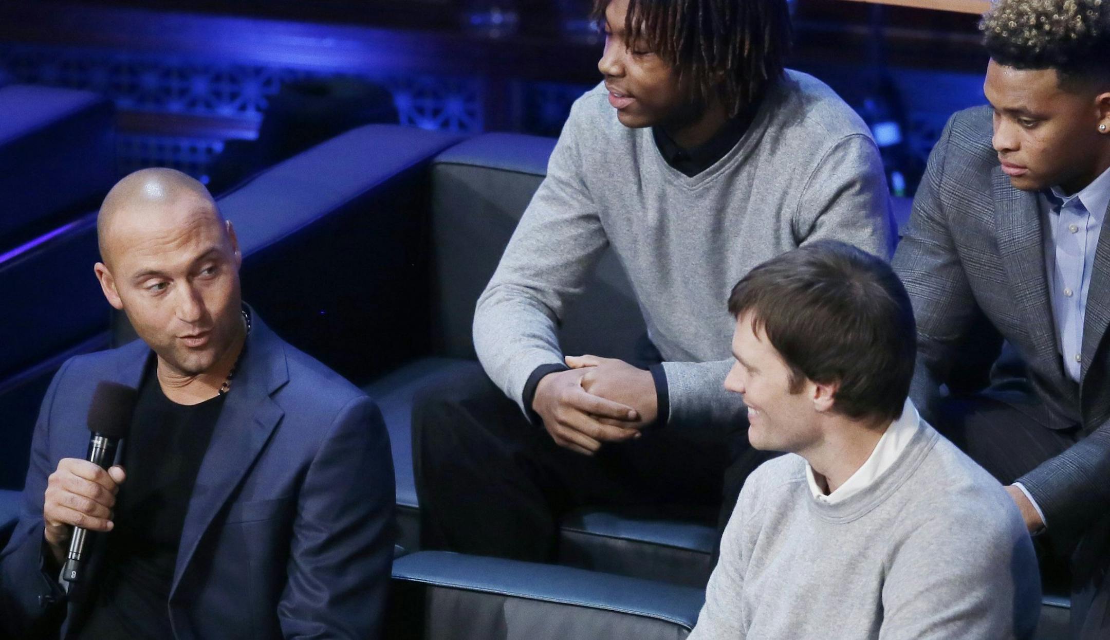 Derek Jeter, left, talks with former Michigan school quarterback Tom Brady and Michigan football coach Jim Harbaugh, right, as new recruits Kingston Davis, top right, and Ahmir Mitchell listen in, during the Signing With the Stars spectacle, Wednesday, Feb. 3, 2016 in Ann Arbor, Mich. (AP Photo/Carlos Osorio)
