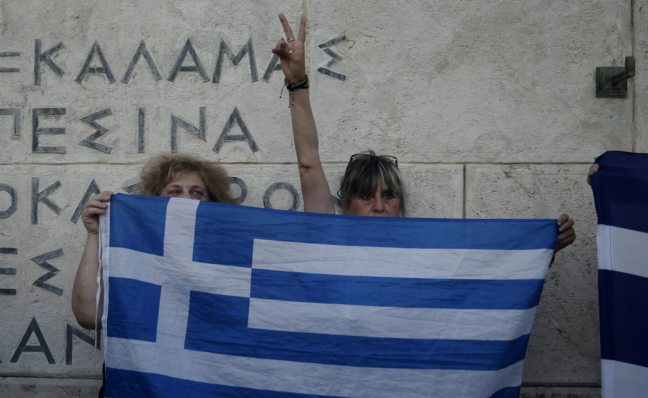 Anti-austerity protesters hold a Greek flag during a rally against the government's agreement with its creditors in front of the tomb of the unknown soldier in Athens, Monday, July 13, 2015. After months of acrimony, Greece clinched a preliminary bailout agreement with its European creditors on Monday that will, if implemented, secure the country's place in the euro and help it avoid financial collapse. (AP Photo/Petros Giannakouris) ORG XMIT: MIN2015071712413434