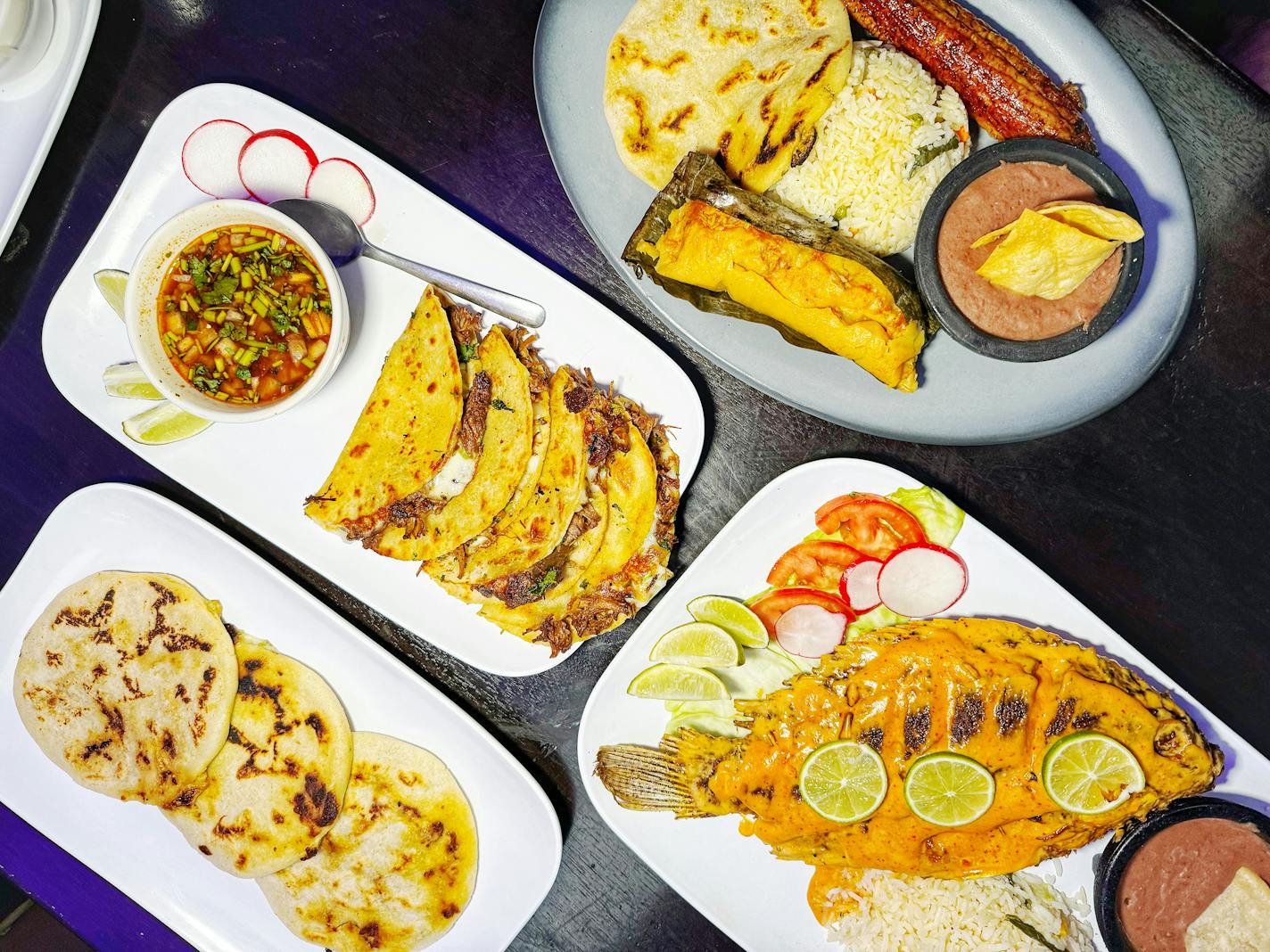 A table with a spread of Salvadorian dishes, including flautas, whole fried tilapia, tacos and pupusas from Abi's Restaurant in Minneapolis.