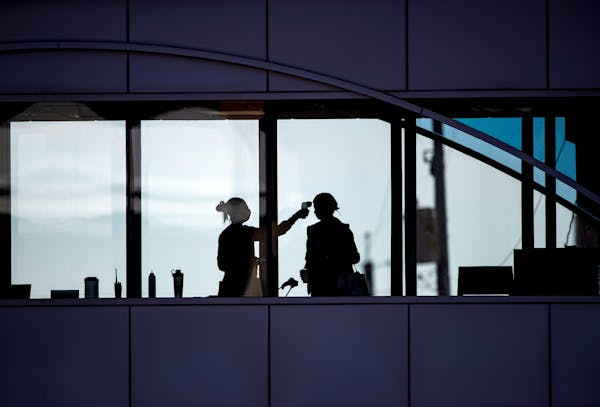 A health care worker takes the temperature of a visitor to Essentia Health who was crossing over a skywalk bridge from the adjoining parking deck in D