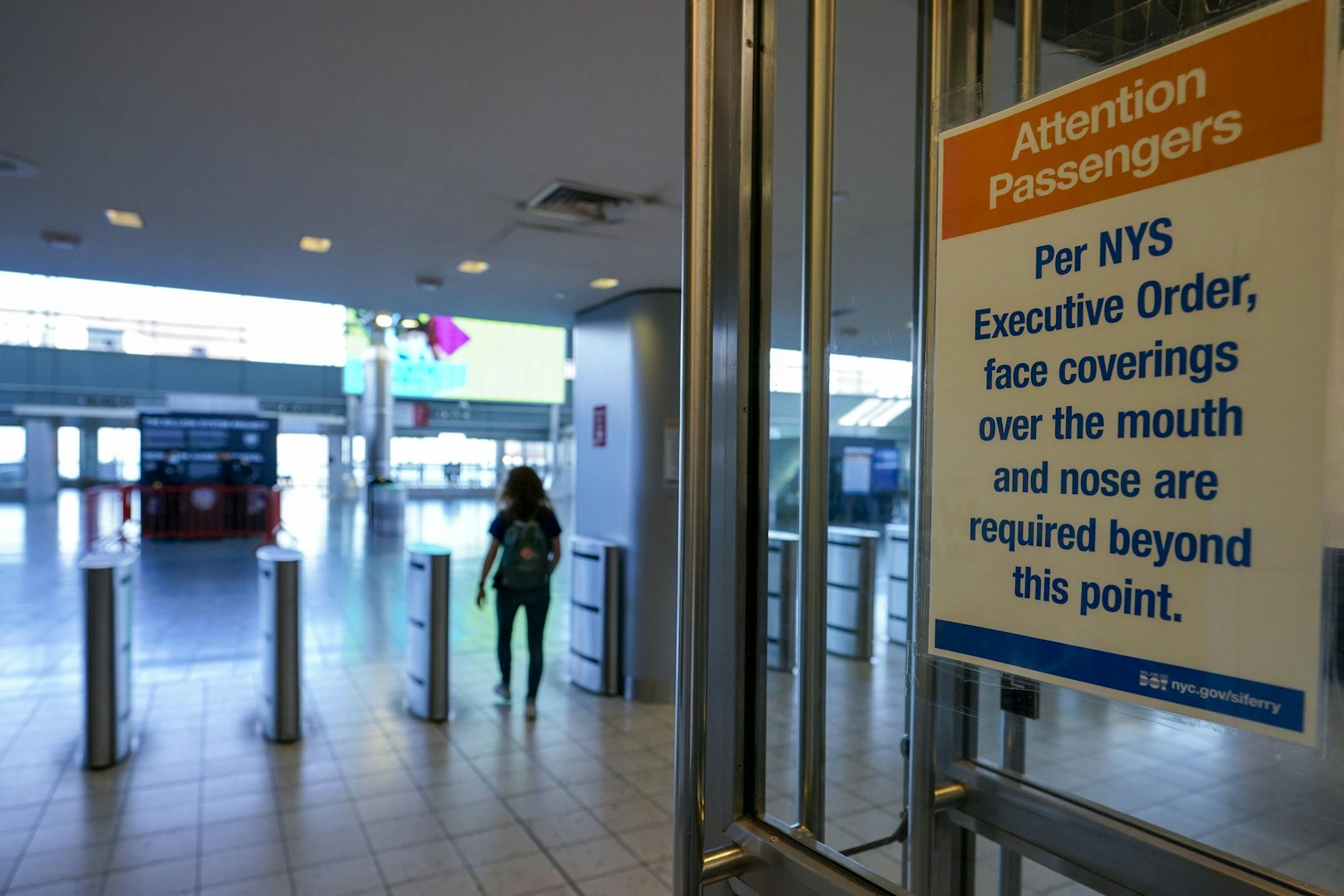 A sign advising passengers that face masks are required hangs on the entrance to the Staten Island ferry waiting room as a commuter runs to catch the ferry, Tuesday, Nov. 10, 2020, in New York. New York City officials are raising awareness and its efforts in stemming a rise in COVID-19 on Staten Island. (AP Photo/Mary Altaffer)