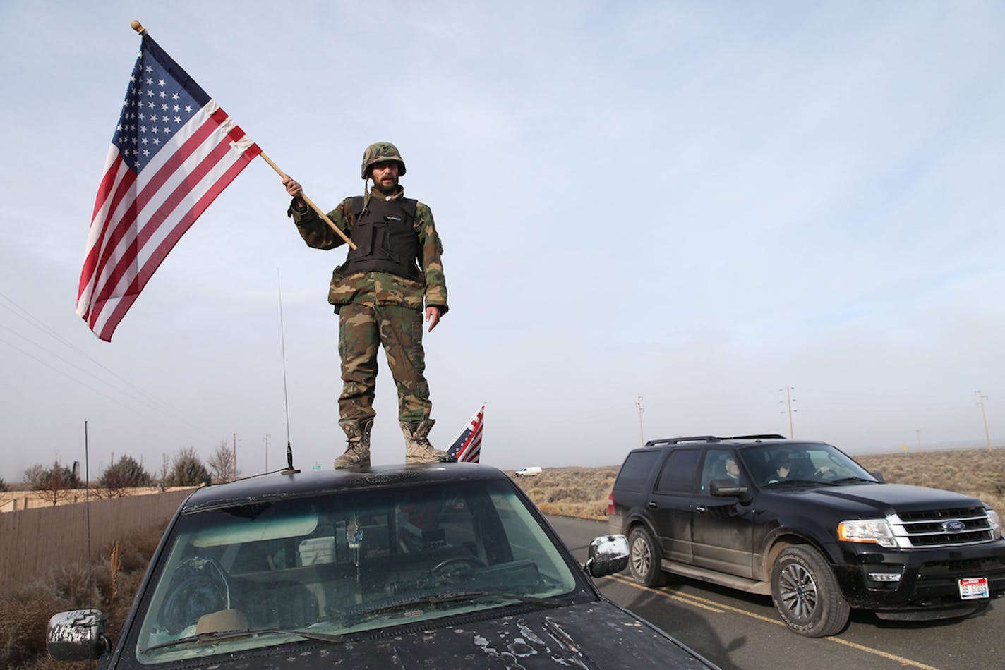 A man waved a U.S. flag from atop a car at the Narrows roadblock, Thursday, Feb. 11, 2016, near Burns, Ore.