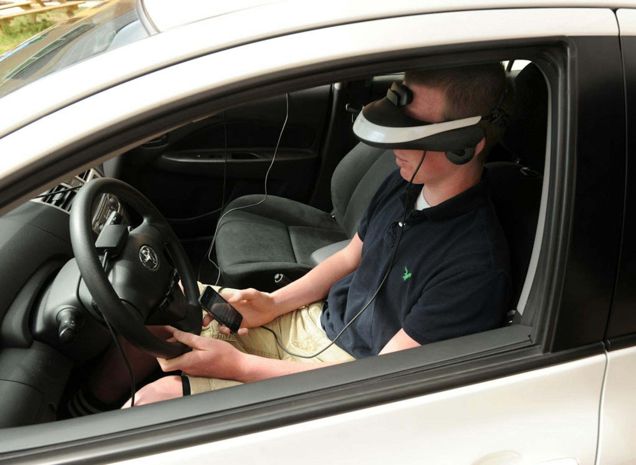 Wearing a headset that projects a street scene, Tyler Hagedorn, a freshman at North High School, tries to text with his cell phone in his lap while driving during a simulation at the school on May 7, 2013.