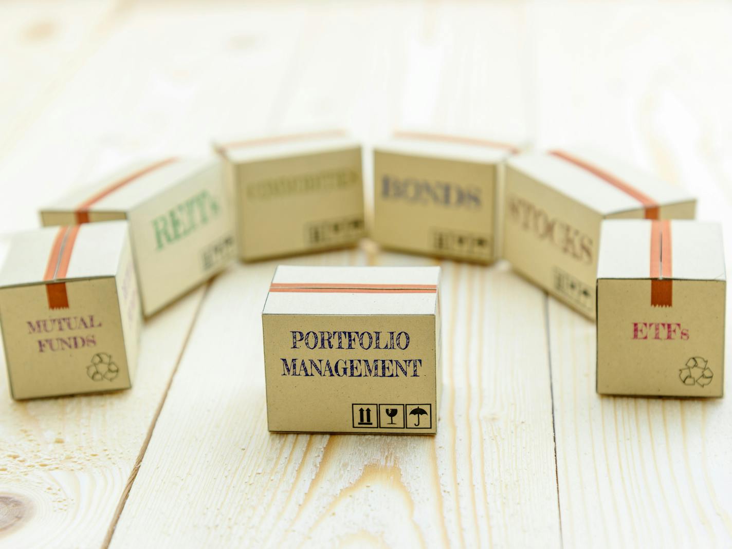 Portfolio and wealth management with risk diversification concept : Small paper cartons / boxes of financial instruments i.e ETFs, REITs, stocks, bonds, mutual funds and commodities, on a wood table.