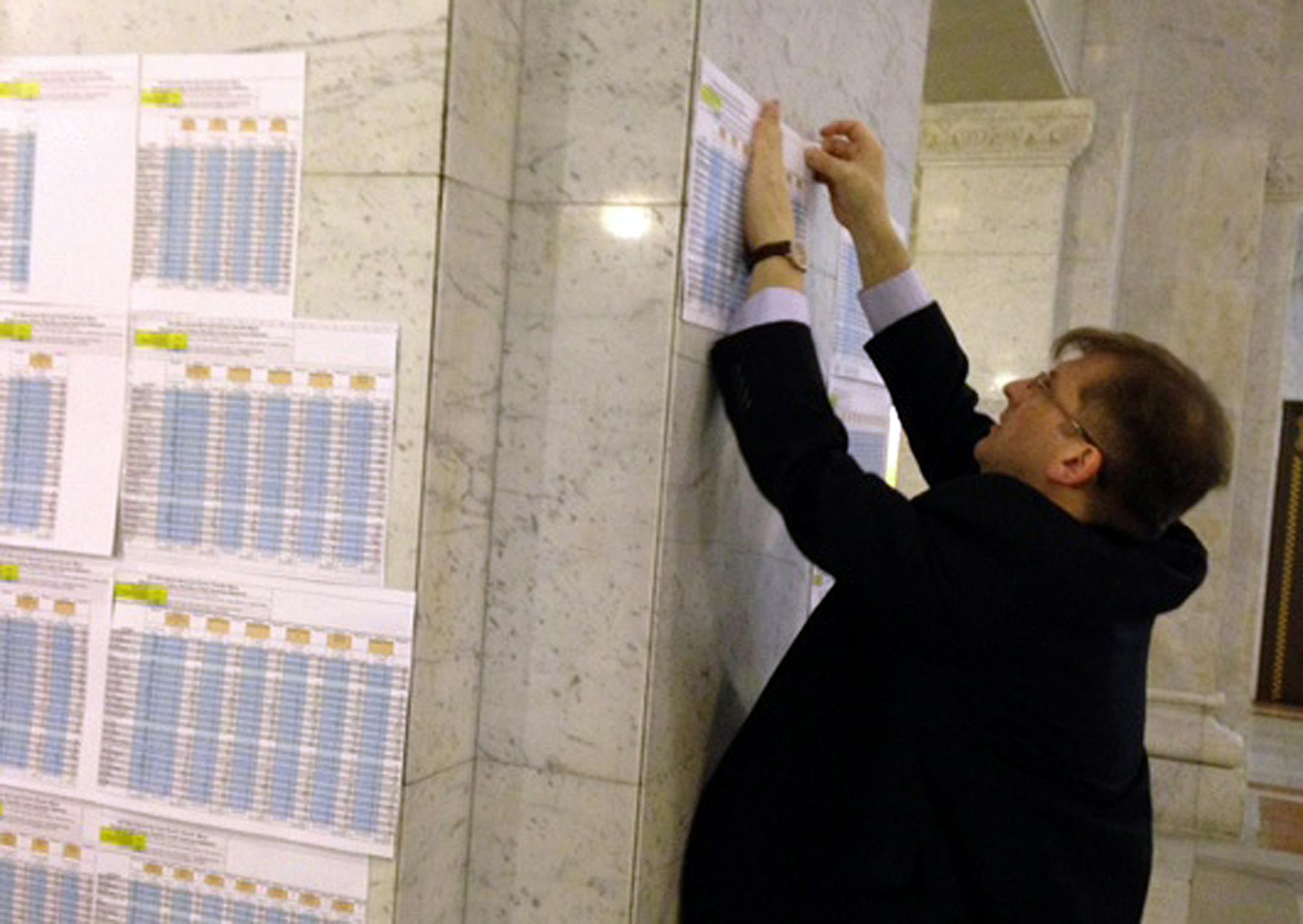 City clerk Casey Carl makes room on a City Hall pillar for another spreadsheet after the 16th round of ranked-choice mayoral vote-counting on Thursday.