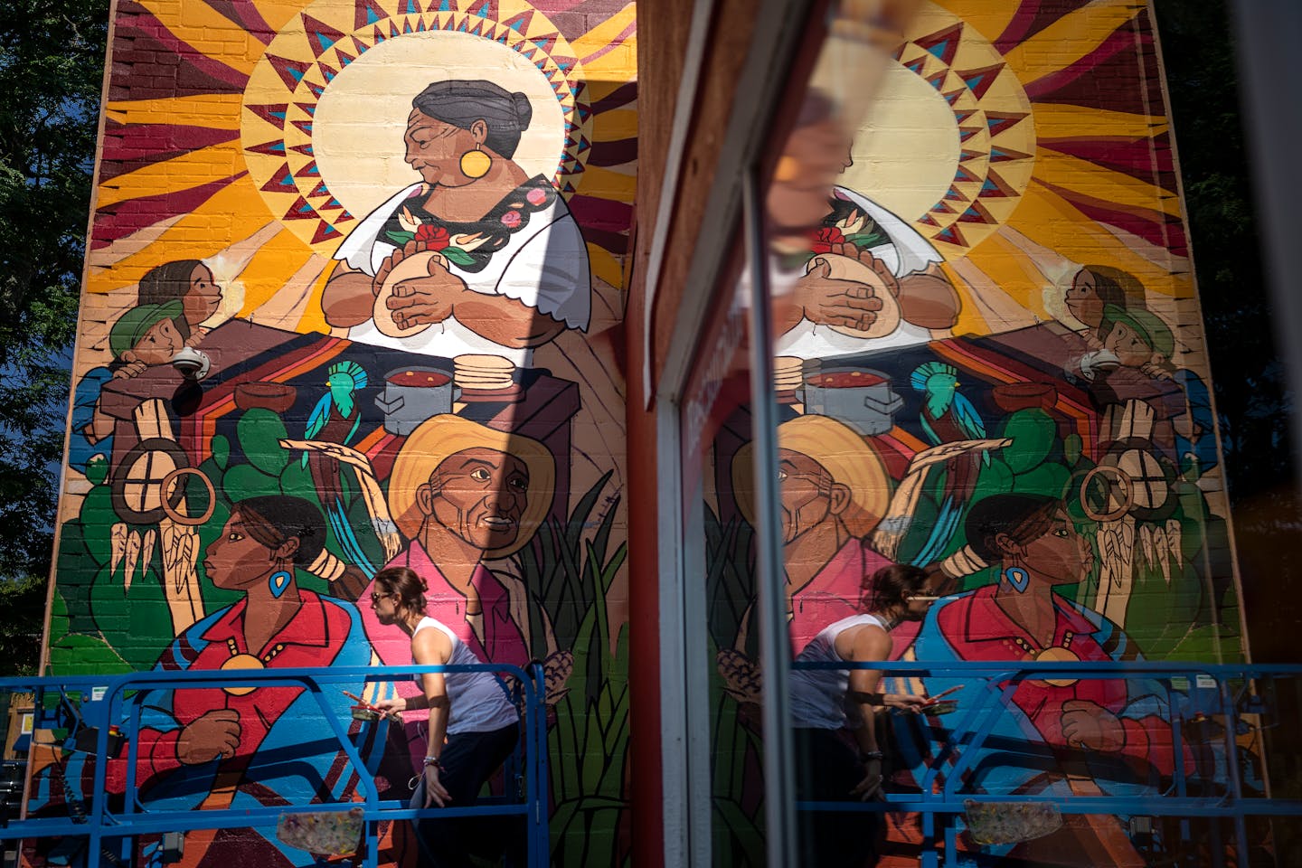 Artist Daniela Bianchini at left, painted a mural called "Legends of Identity" on the outside wall of El Burrito Mercado Monday. The mural was reflected in the window fo the building.] Jerry Holt •Jerry.Holt@startribune.com