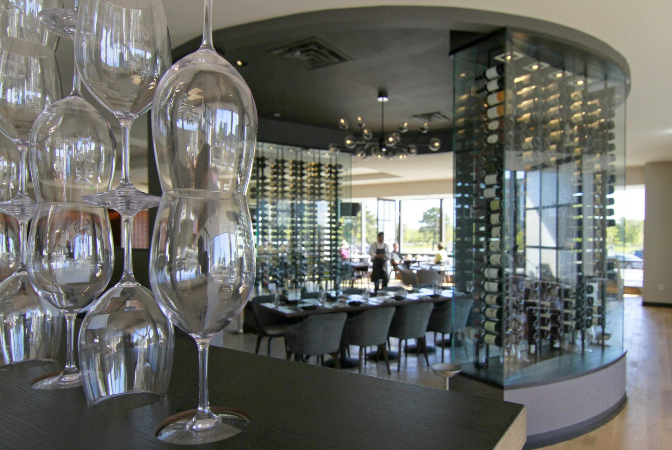 Interior, a divider of wine glasses seperates the bar area and the dining room, with a group table situated inside see-through wine racks