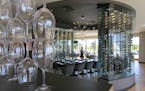 Interior, a divider of wine glasses seperates the bar area and the dining room, with a group table situated inside see-through wine racks