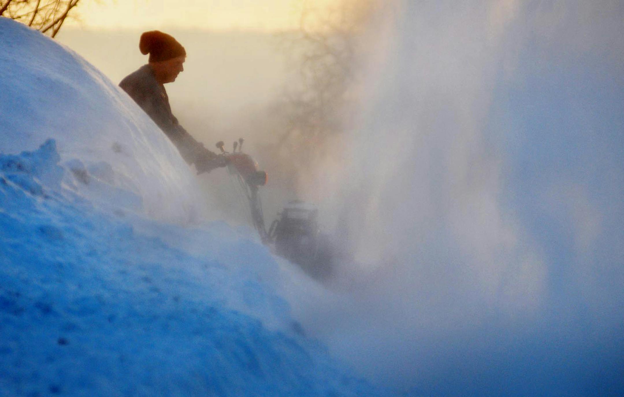 John Nadeau of St. Peter, Minn., already is literally up to his ears in snow as, at dawn's early light, he battles yet another snowfall, Wednesday, March 5, 2014.