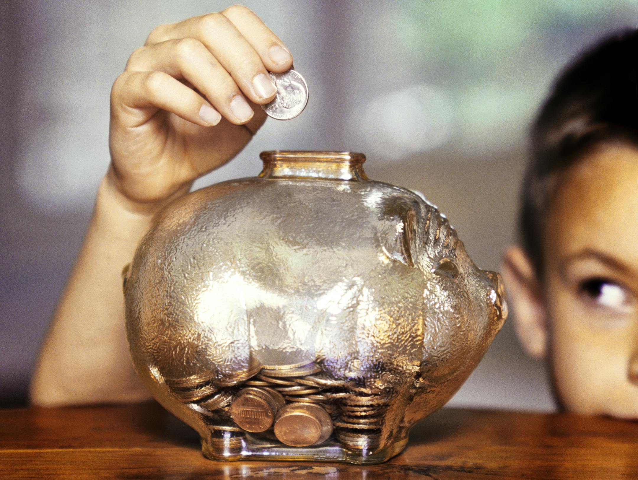 Little boy adding coins to glass piggy bank.