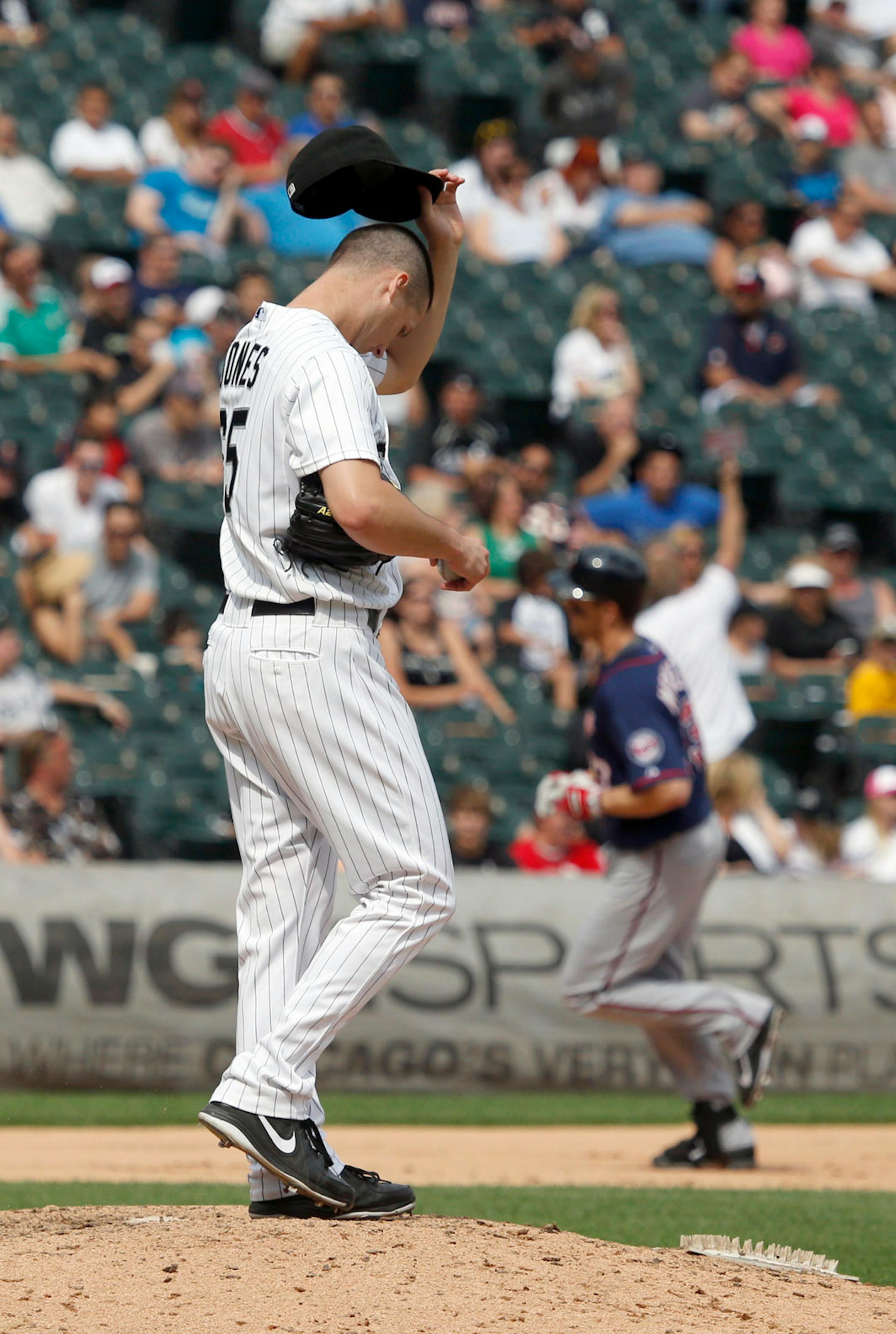 Chicago White Sox relief pitcher Nate Jones, left, wipes his face after giving up a grand slam to Minnesota Twins' Justin Morneau, rear right, during the seventh inning of a baseball game Friday, Aug. 9, 2013, in Chicago. Joe Mauer, Clete Thomas, and Pedro Florimon also scored on the play.