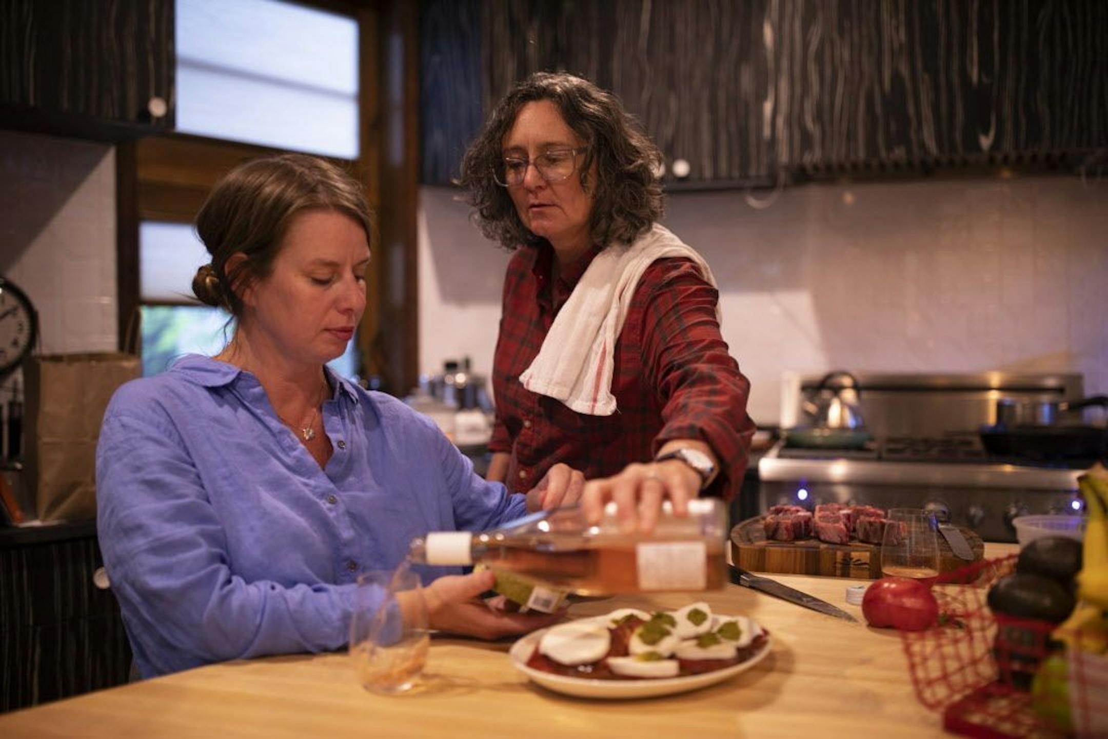 Kim Bartmann reached across her wife, Sarah Jane Wroblewski, to refill her glass of rose while they fixed dinner.
