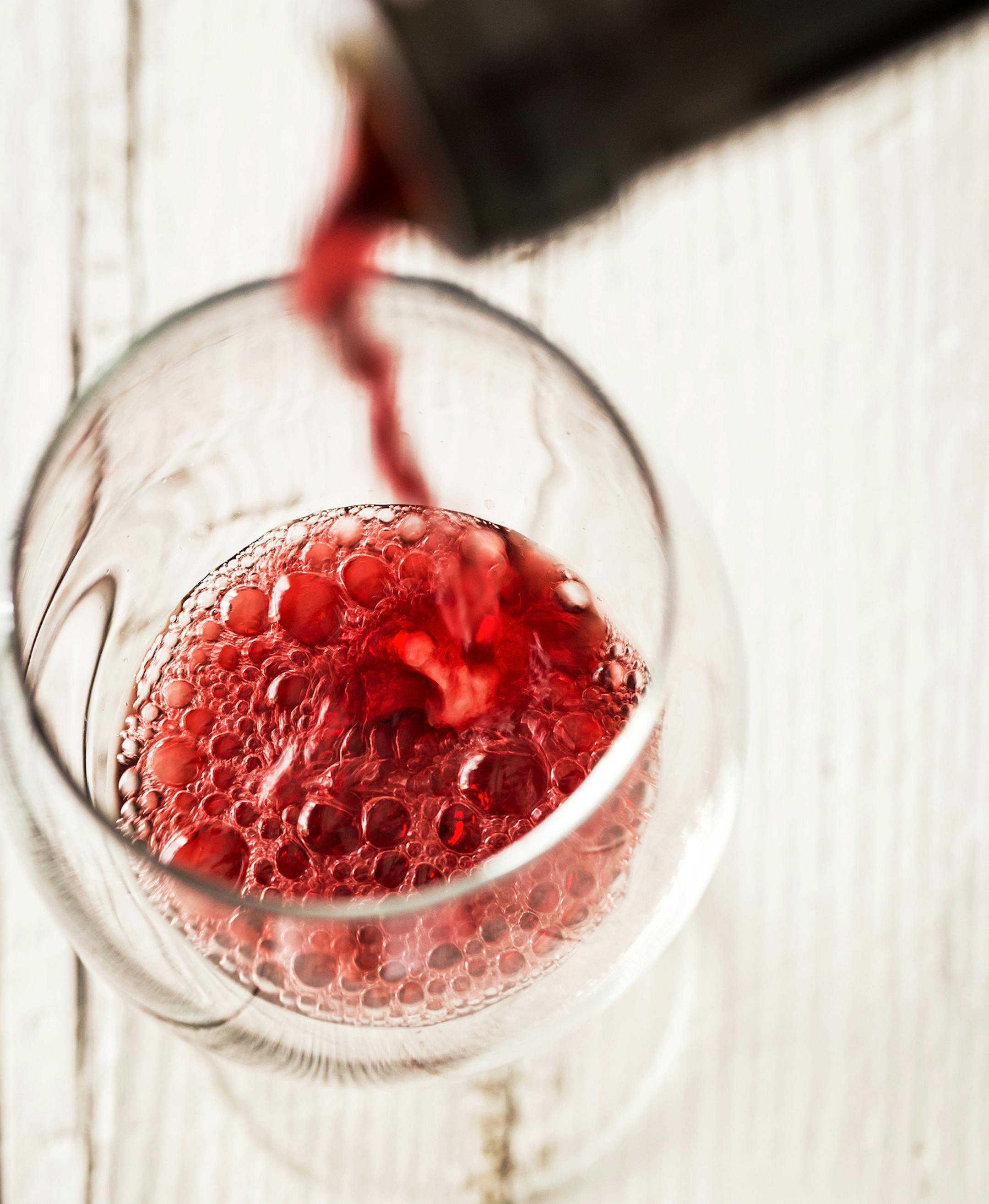 Pouring red wine into the glass crystal white wooden table from istock