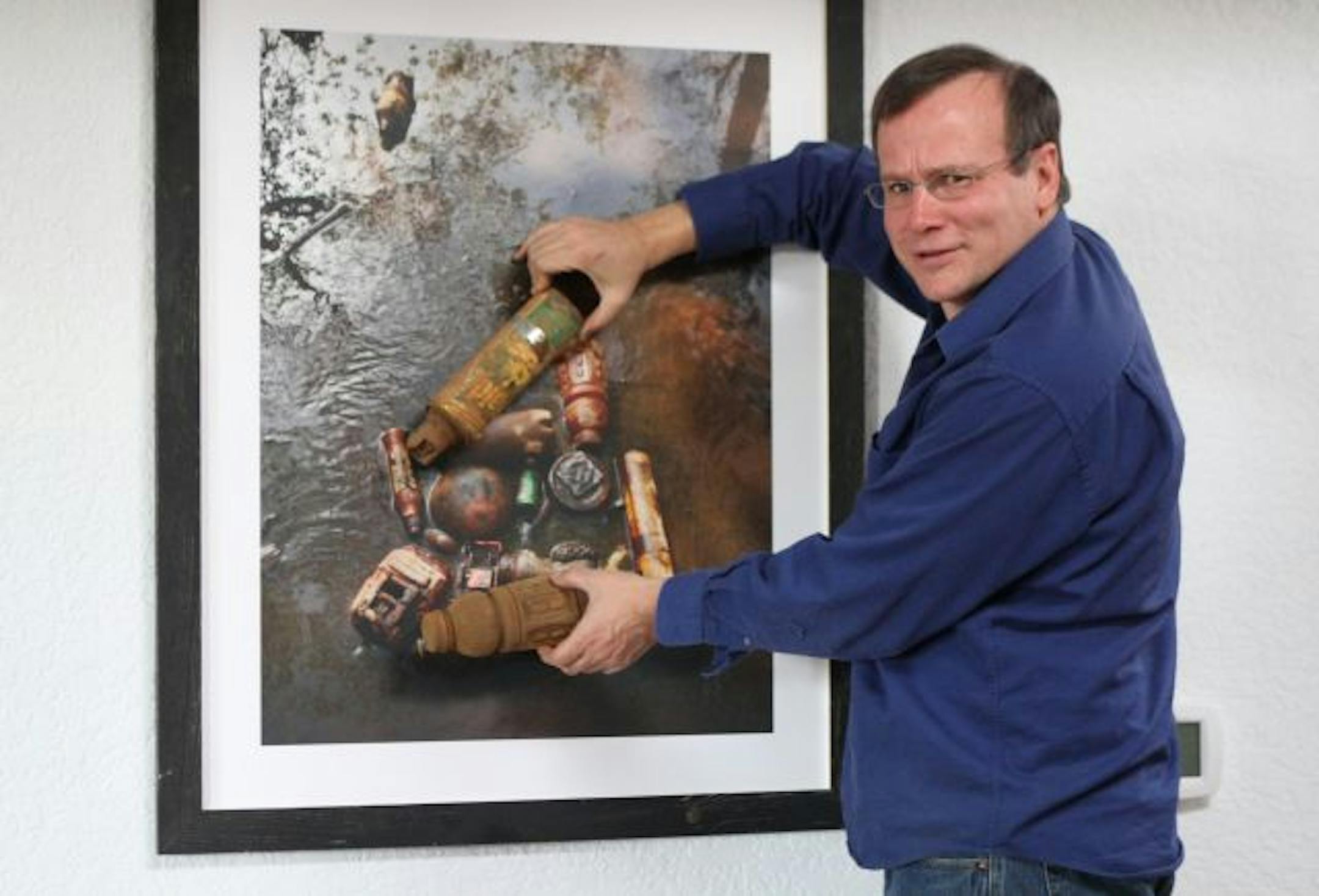 Artist Peter L. Johnson held a rusty can of Raid and a Gatorade bottle up to the photograph he took of them alongside other trash he picked up on Earth Day. This image was one of two that he sent to city officials to help make his case that an inspection was warranted.