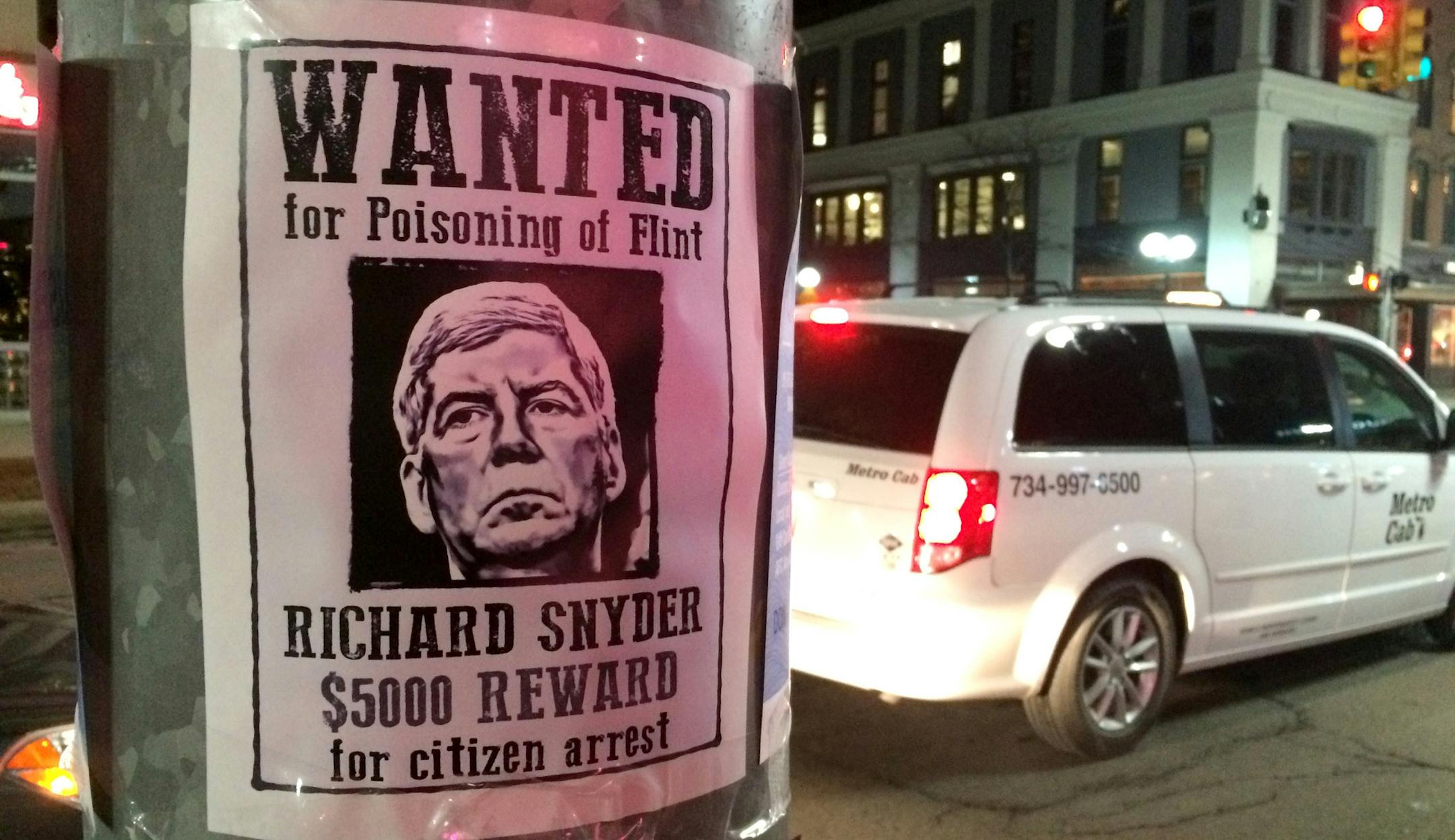In this photo taken on Wednesday, Jan. 27, 2016, a poster offering a $5,000 reward for "citizen arrest" of Michigan Gov. Rick Snyder is displayed in downtown Ann Arbor, Mich. The posters were among messages criticizing Snyder, including ones written in chalk on sidewalks, over his handling of the water crisis in Flint, Michigan. (Ryan Stanton /The Ann Arbor News via AP) LOCAL TELEVISION OUT; LOCAL INTERNET OUT; MANDATORY CREDIT