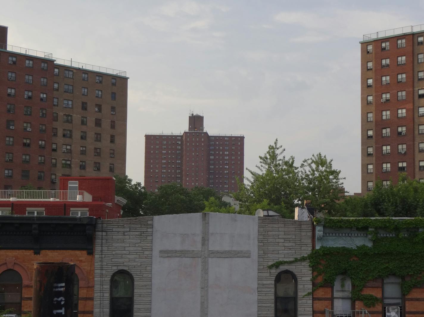 Brick apartment buildings in Bed-Stuy, Brooklyn, New York City, rising behind cross on a church facade