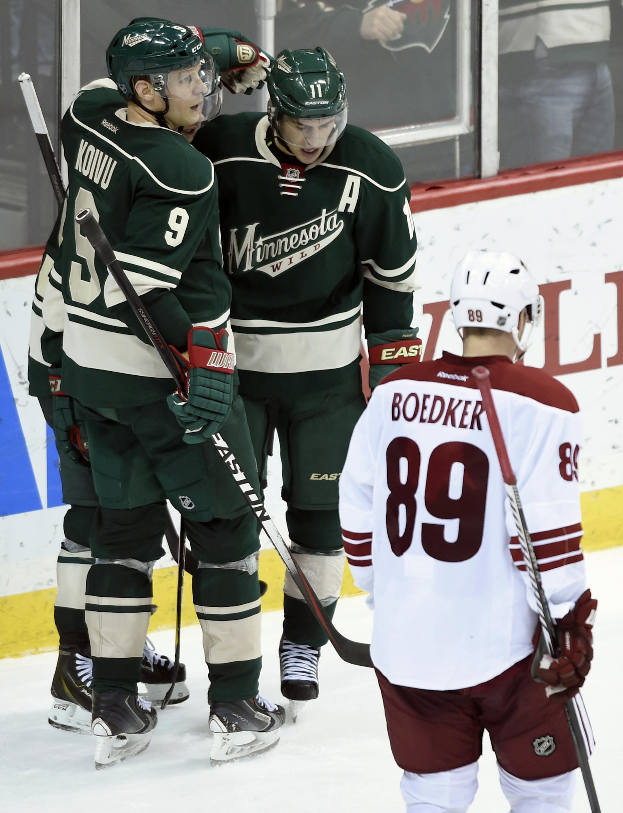 Arizona Coyotes left wing Mikkel Boedker (89), of Denmark, skates past as Minnesota Wild center Mikko Koivu (9) and right wing Jason Pominville (29) congratulate left wing Zach Parise (11) on an empty-net goal during the third period of an NHL hockey game Saturday, Jan. 17, 2015, in St. Paul, Minn. The Wild won 3-1. (AP Photo/Hannah Foslien)