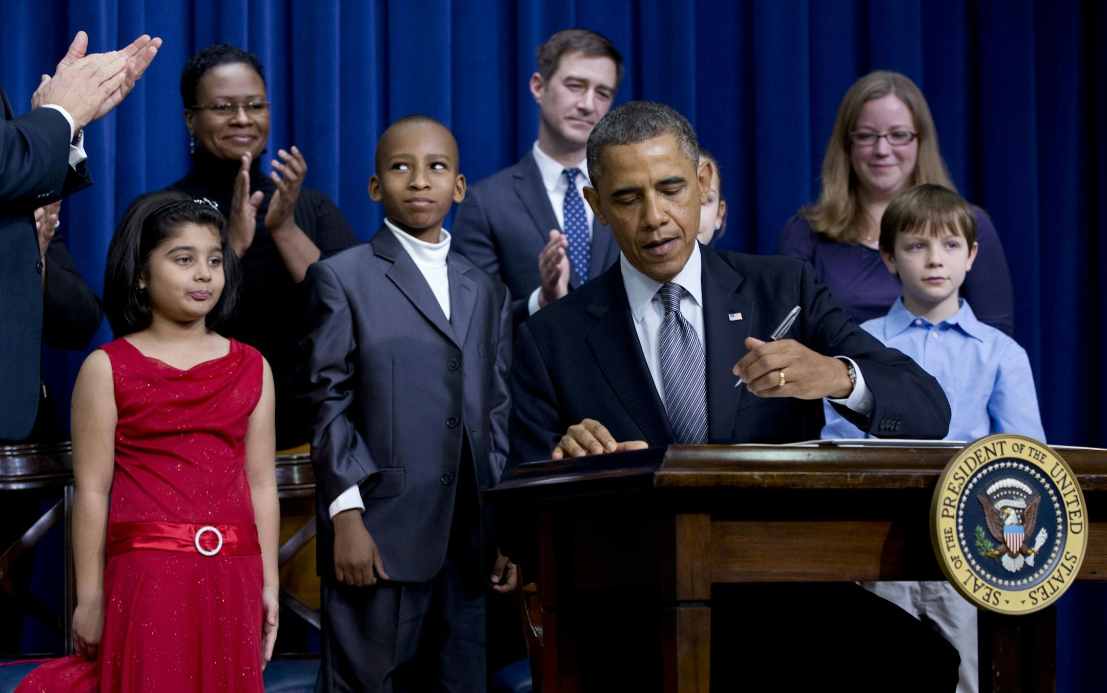 President Barack Obama, accompanied by Vice President Joe Biden, standing left clapping, and children who wrote the president about gun violence following last month's shooting at an elementary school in Newtown, Conn., signs executive orders to reduce gun violence, Wednesday, Jan. 16, 2013.