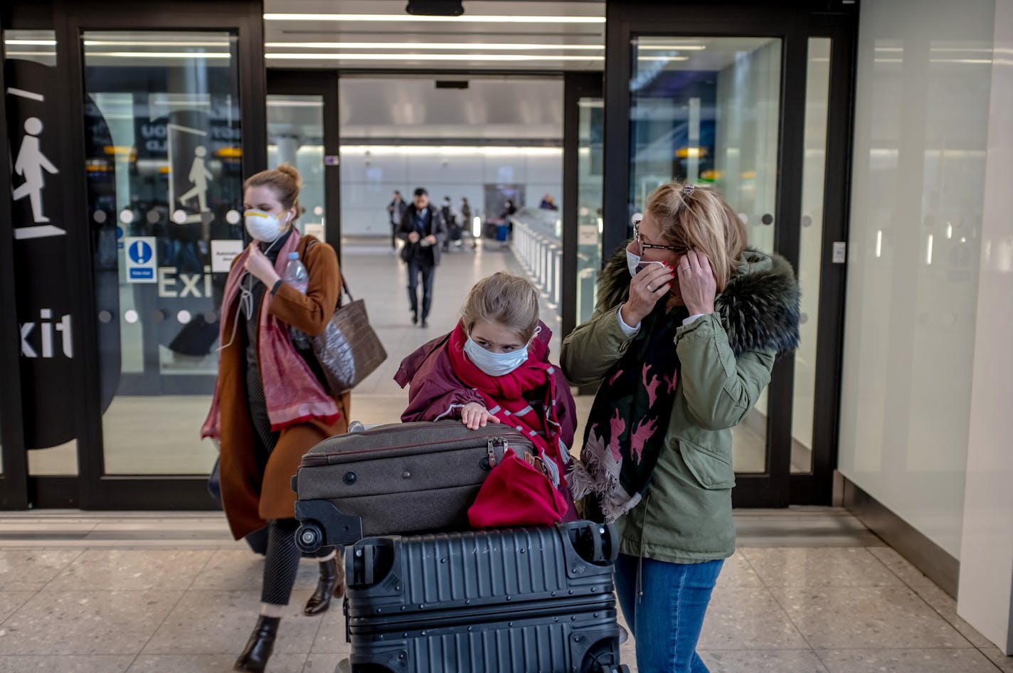 A woman helps her young daughter put on a face mask as they arrive at London's Heathrow Airport, for their flight on Friday, March 13, 2020. Concerns over the coronavirus has caused many people to cancel their flight plans. (Andrew Testa/The New York Times)