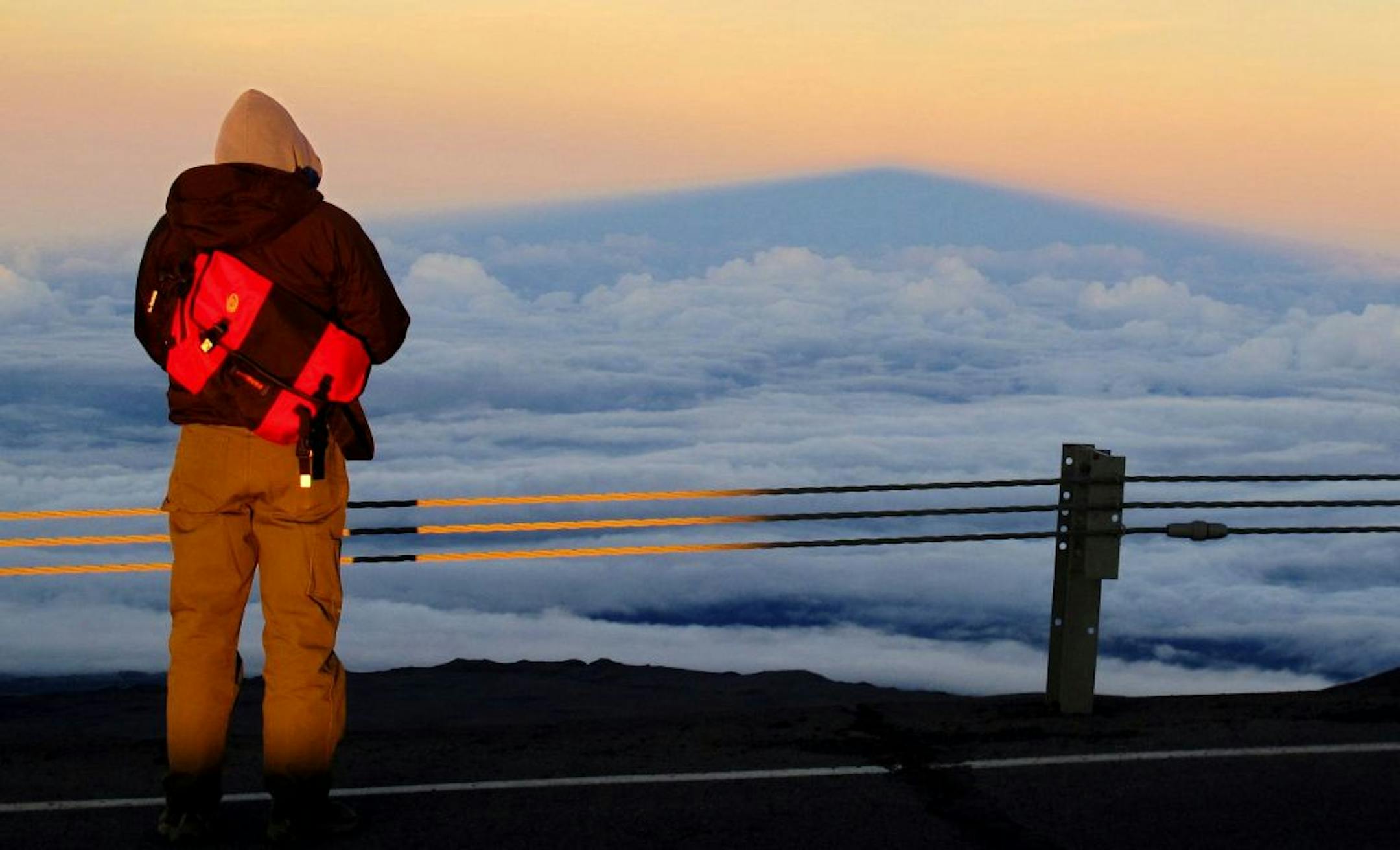 A summit visitor looks eastward to the shadow of Hawaii's Mauna Kea cast against clouds at sunset.