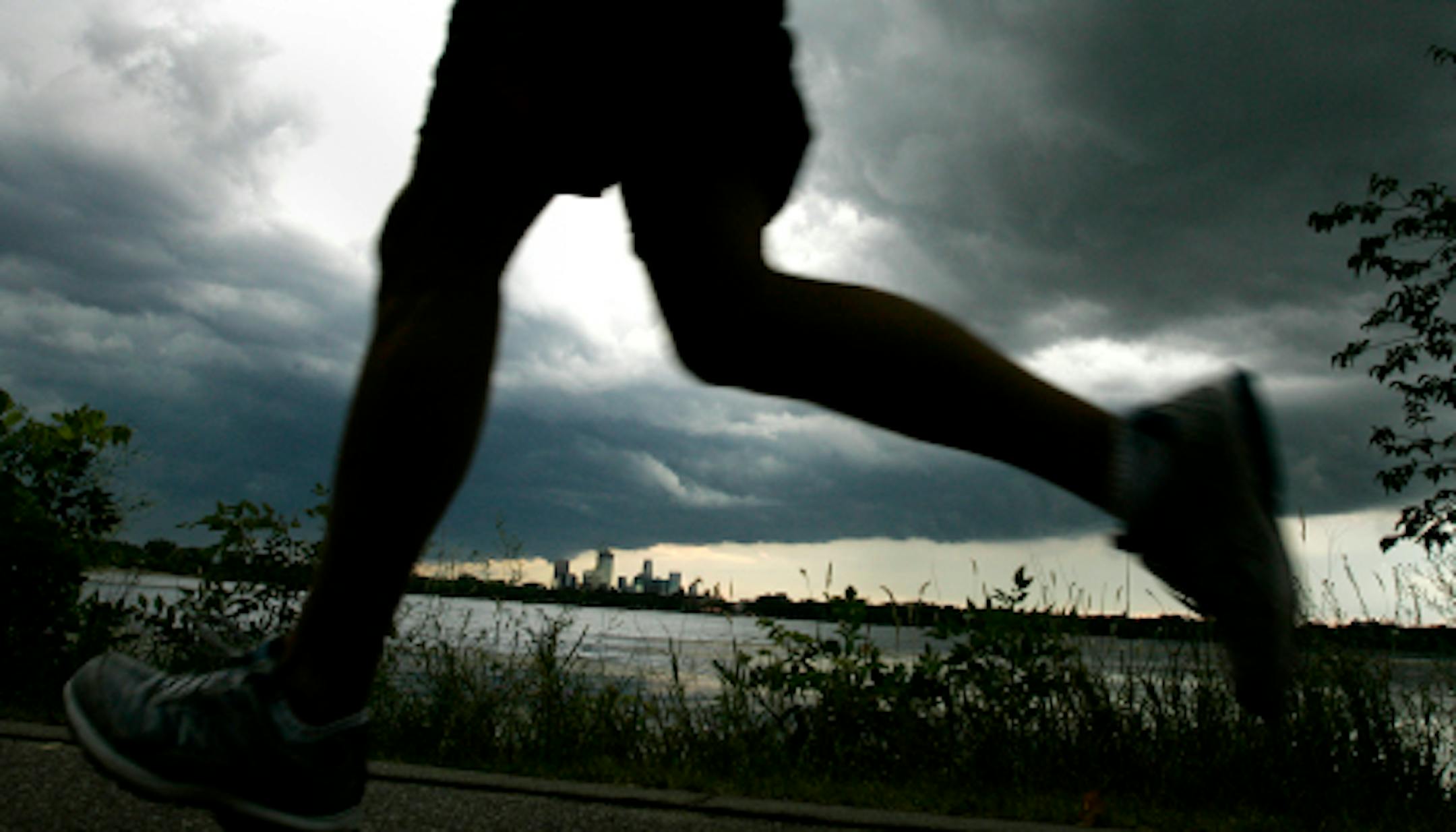 DAVID JOLES ' djoles@startribune.com Minneapolis, MN - July 21, 2009-] Ominous looking storm clouds hang over downtown Minneapolis, as a runner heads around Lake Calhoun.