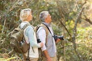 cheerful middle aged couple bird watching in forest. istock