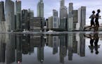 In this Thursday, Jan. 25, 2018, file photo, the financial skyline of Singapore is reflected in a rain puddle as people jog past at dawn in Singapore.