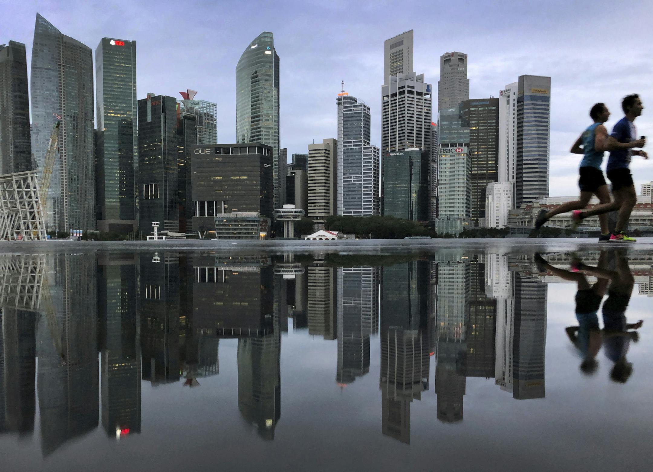 In this Thursday, Jan. 25, 2018, file photo, the financial skyline of Singapore is reflected in a rain puddle as people jog past at dawn in Singapore. (AP Photo/Wong Maye-E, File) ORG XMIT: ASIA508