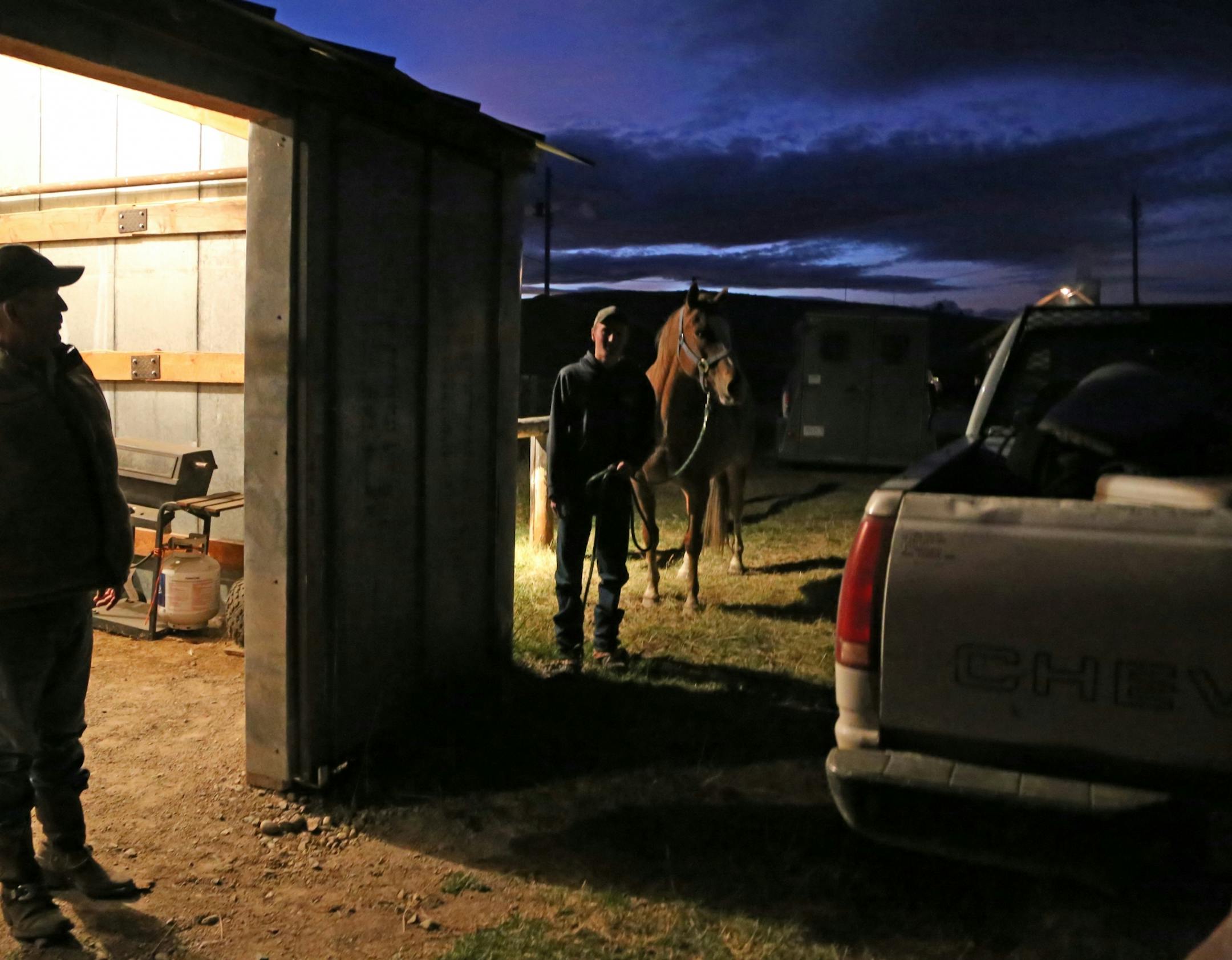 Mike Krause, left, of South Haven, Minn., is silhoutted in the doorway of a shed where saddles and other tack are kept after riders return from the Montana mountains following long days of gathering cattle on U.S. Forest Service units measuring 13,000 acres. The cattle are part of a ranching operation near Wisdom, Mont., owned by brothers Clay and Dean Peterson. Krause, who competes in the Midwest on cutting horses, hauls his own stock from Minnesota to Montana to help with the roundup. Dayton S