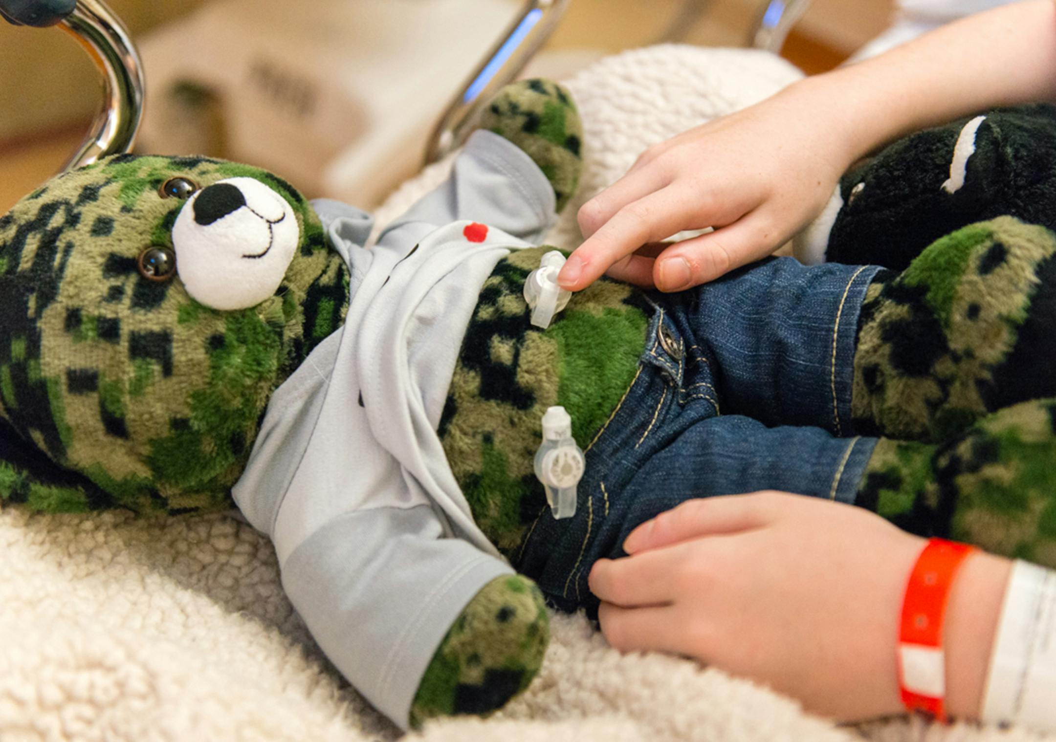 Matthew Husby, 9, points to the gastrostomy tube on his teddy bear that is similar to the one he has inserted in his stomach. (Heidi de Marco/Kaiser Health News/TNS)