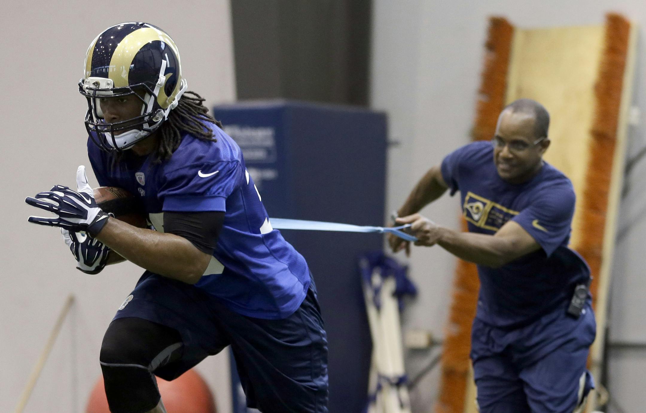 St. Louis Rams running back Todd Gurley, left, runs with the ball as he is pulled back by a trainer during an NFL football organized team activity, Thursday, June 4, 2015, in St. Louis. (AP Photo/Jeff Roberson) ORG XMIT: MOJR
