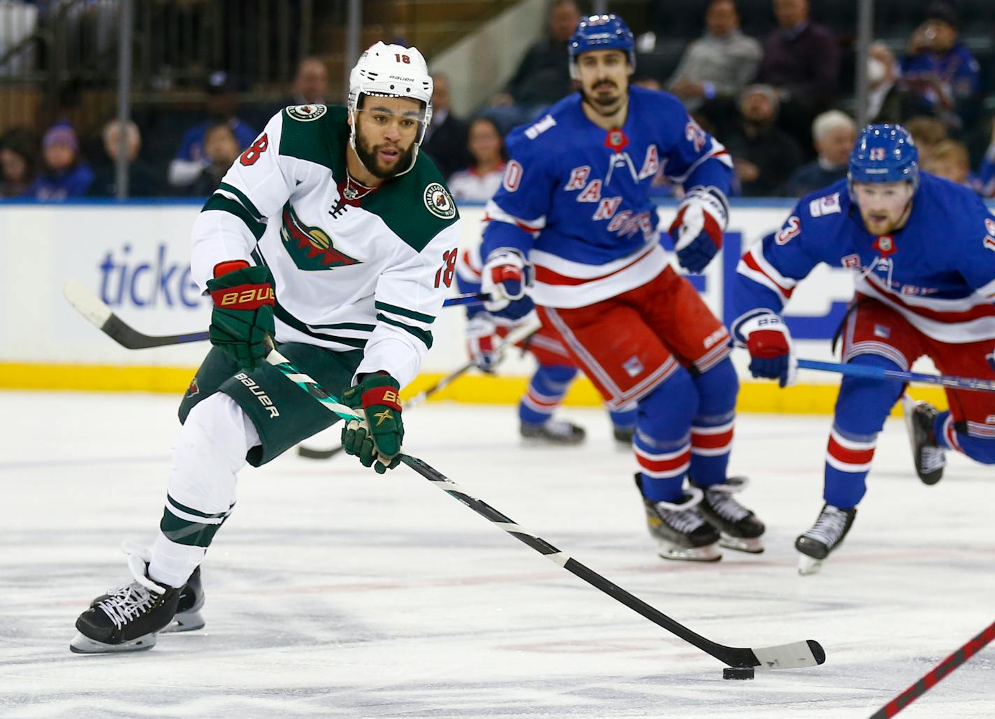 Minnesota Wild's Jordan Greenway (18) skates up ice with the puck while being trailed by New York Rangers' Chris Kreider (20) and Alexis Lafreniere (13) during the second period of an NHL hockey game Friday, Jan. 28, 2022, in New York. (AP Photo/John Munson)