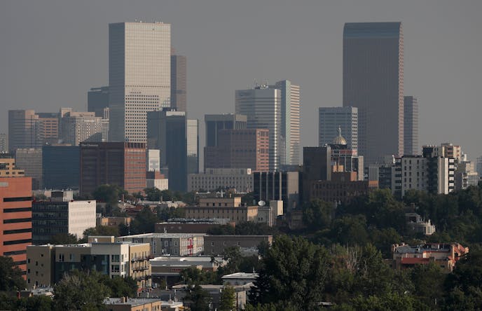 A smoky haze envelopes the skyscrapers and Rocky Mountains that usually can be seen as a backdrop to the city from a high-rise building Monday, Aug. 20, 2018, in Denver. Smoke from the countless wildfires burning in western Canada as well as the American West has forced the issuance of air quality alerts across the region. (AP Photo/David Zalubowski)