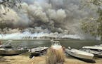Boats are pulled ashore as smoke and wildfires rage behind Lake Conjola, Australia, Thursday, Jan. 2, 2020. Thousands of tourists fled Australia's wil