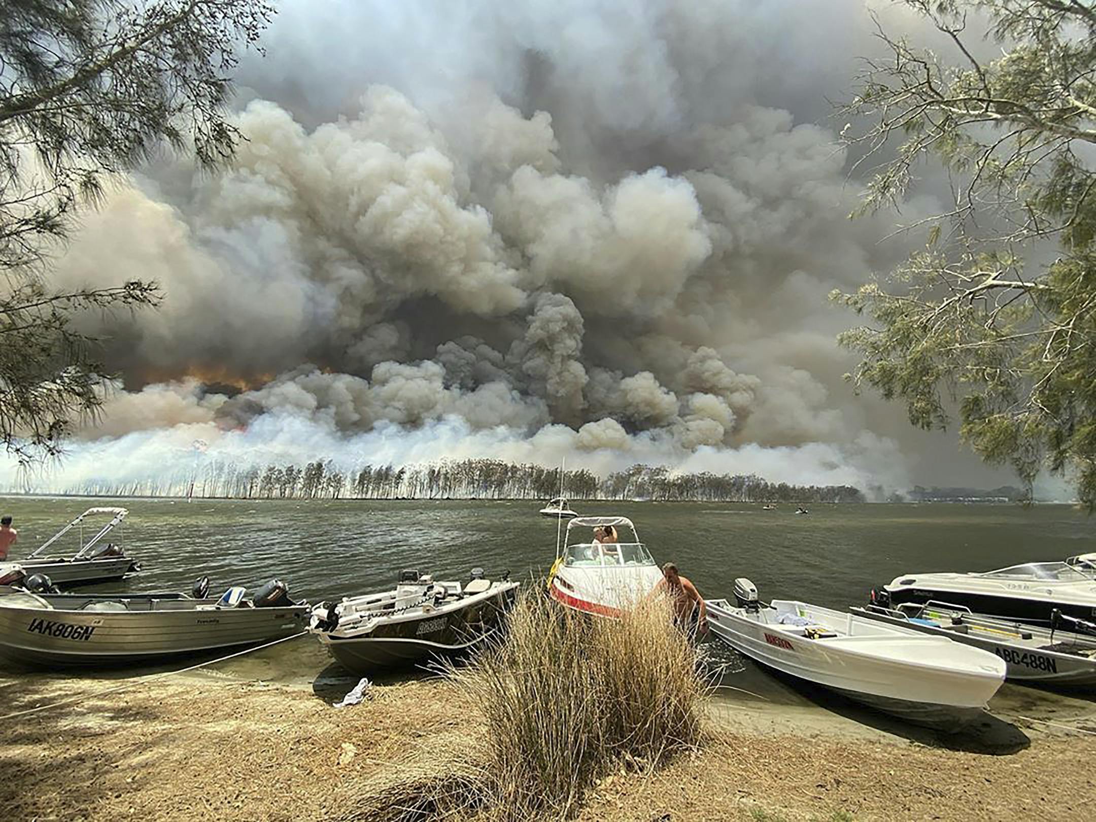 Boats are pulled ashore as smoke and wildfires rage behind Lake Conjola, Australia, Thursday, Jan. 2, 2020. Thousands of tourists fled Australia's wildfire-ravaged eastern coast Thursday ahead of worsening conditions as the military started to evacuate people trapped on the shore further south. (Robert Oerlemans via AP)