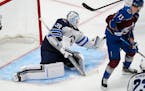 Jets goaltender Laurent Brossoit, left, makes a glove save of a redirected shot by Avalanche right wing Valeri Nichushkin (13) in the third period Sun