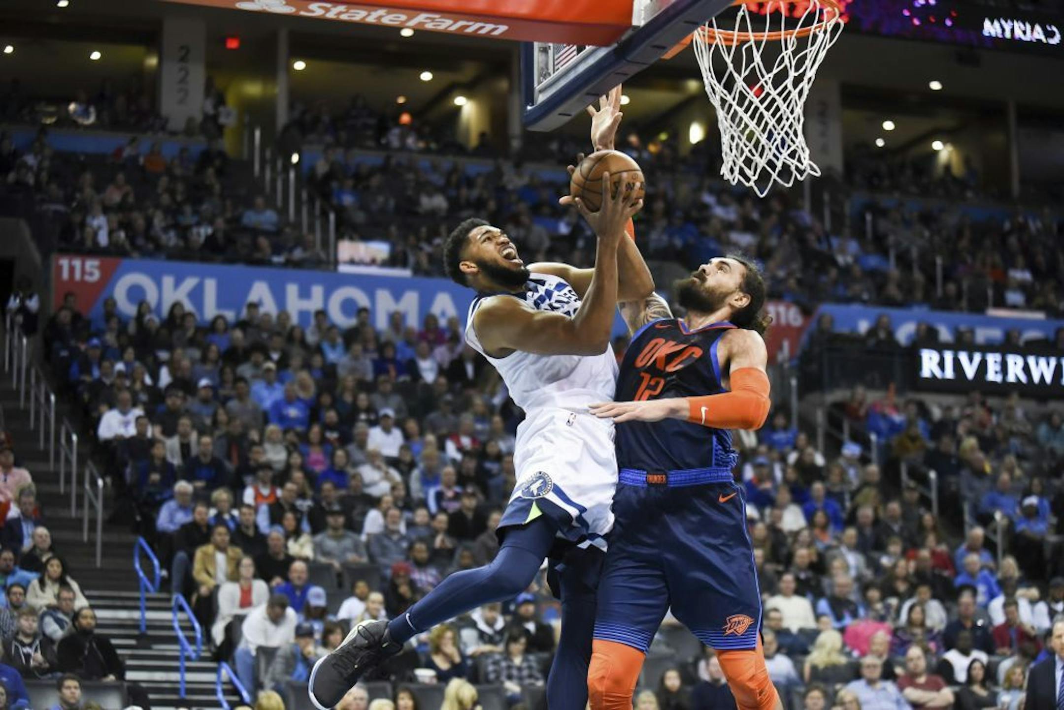 Minnesota Timberwolves center Karl-Anthony Towns, left, goes up to shoot over Oklahoma City Thunder center Steven Adams, right, in the first half of an NBA basketball game in Oklahoma City, Sunday, Dec. 23, 2018.