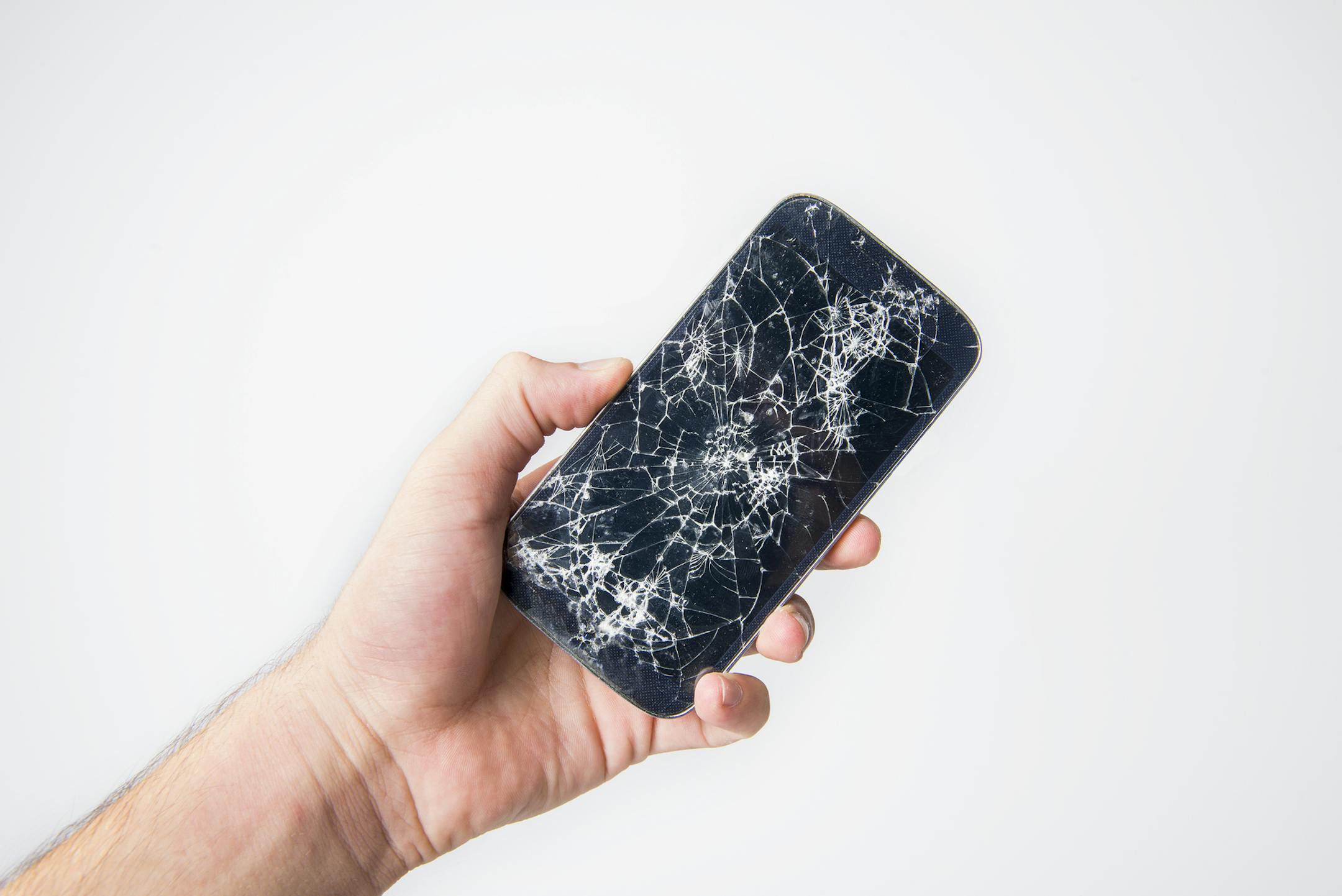 High angle view of unrecognizable person holding a broken smart phone over white background. Horizontal composition. Image taken with Nikon D800 and developed from Raw format.