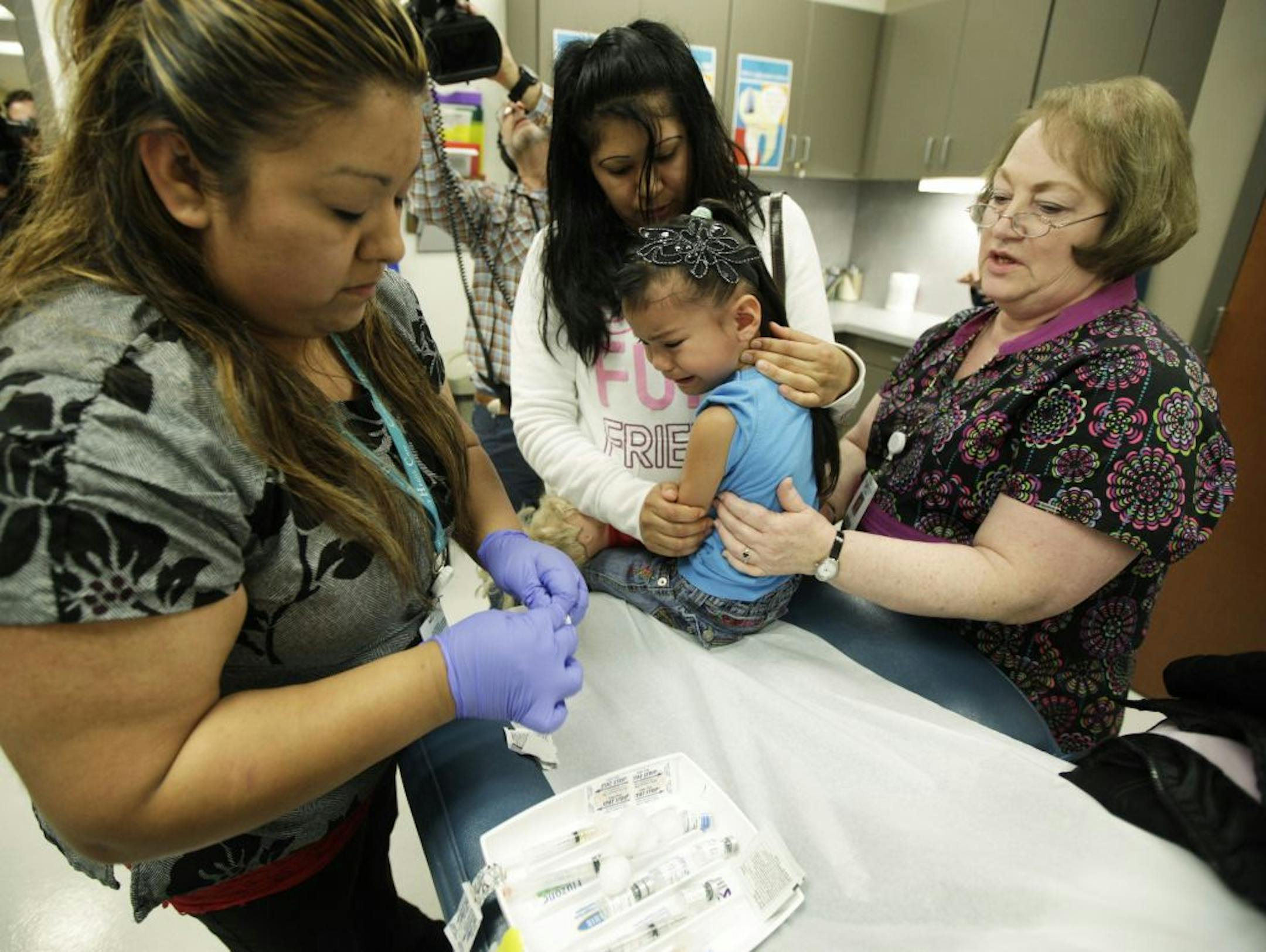 Nurses Fatima Guillen, left, and Fran Wendt, right, give Kimberly Magdeleno, 4, a Tdap whooping cough booster shot, as she is held by her mother, Claudia Solorio, Thursday, May 3, 2012, at a health clinic in Tacoma, Wash. Washington Gov. Chris Gregoire opened up an emergency fund Thursday to help contain a whooping cough epidemic in the state as officials urged residents to get vaccinated.