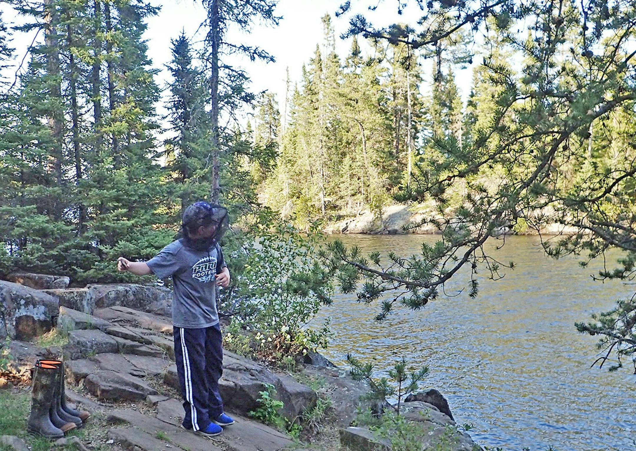 Joe Kennedy, wearing a mosquito head net, skips rocks onto Sawbill Lake from a campsite on the lake's north end. On his first trip ever to the Boundary Waters Canoe Area Wilderness, he built campfires, played with his Buck knife, skipped stones, gathered wood, fished from shore, sat in a hammock and wrote on rocks wth the charcoal end of a fire-tending stick to stay occupied when it was too windy to be in the canoe.